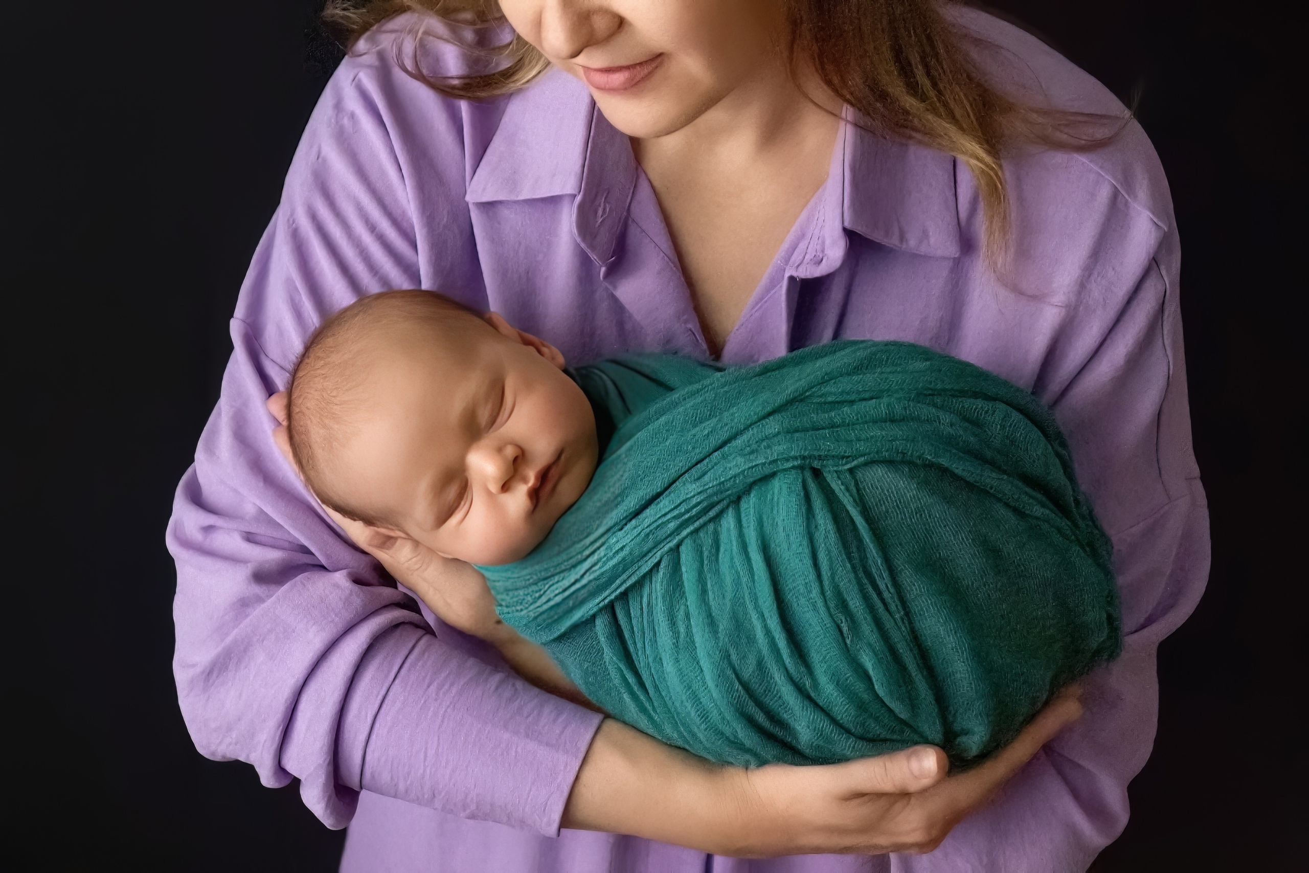 спящий новорожденный ребенок лежит на руках мамы, сиреневая рубашка, зеленая марля, черный фон, дневной свет