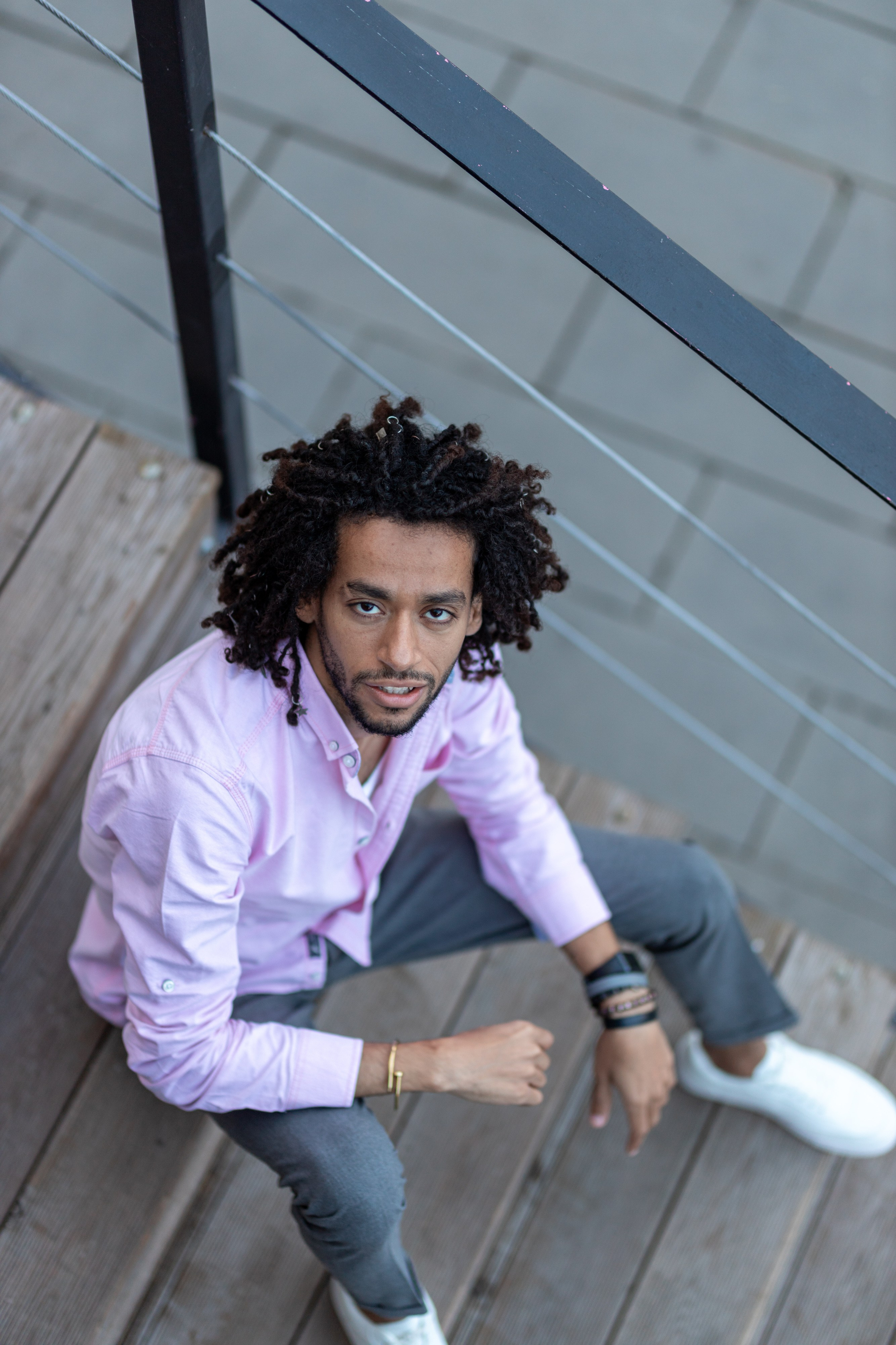 Темнокожий парень в брюках и розовой рубашке сидит на лестнице