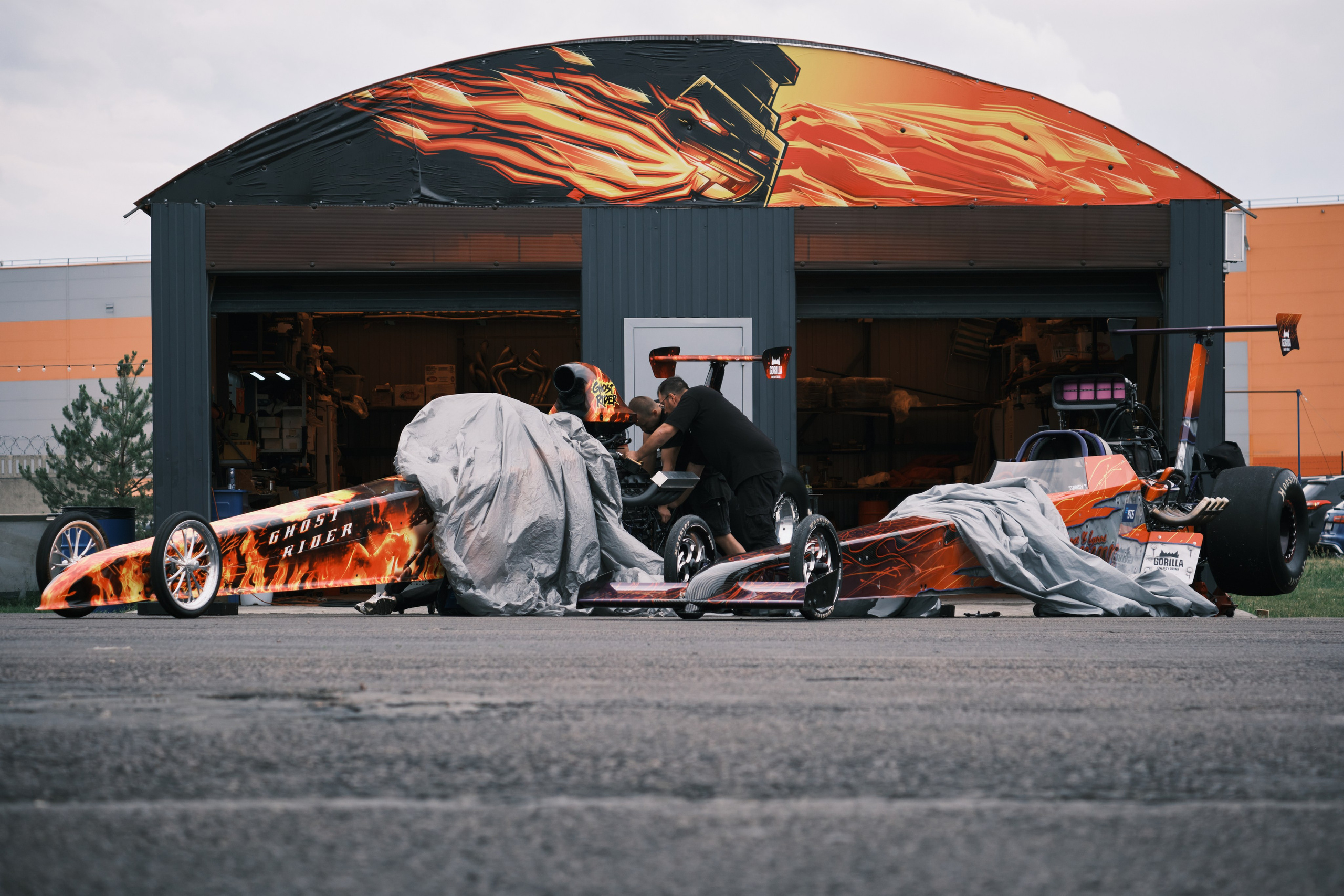 Механики обслуживают два Dragstera на фоне гаража прикрытые чехлами