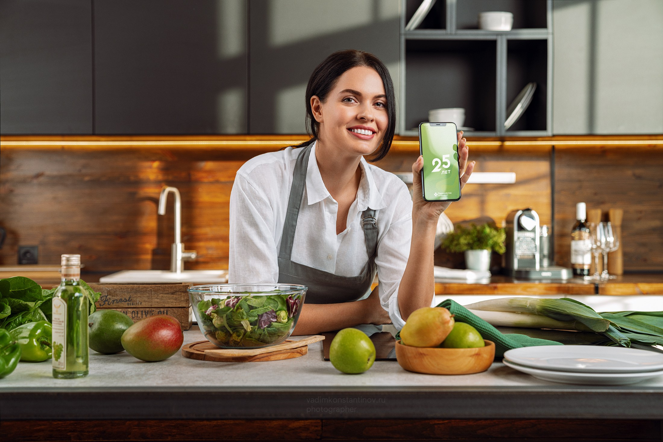 Девушка на кухне в фартуке демонстрирует телефон с приложением