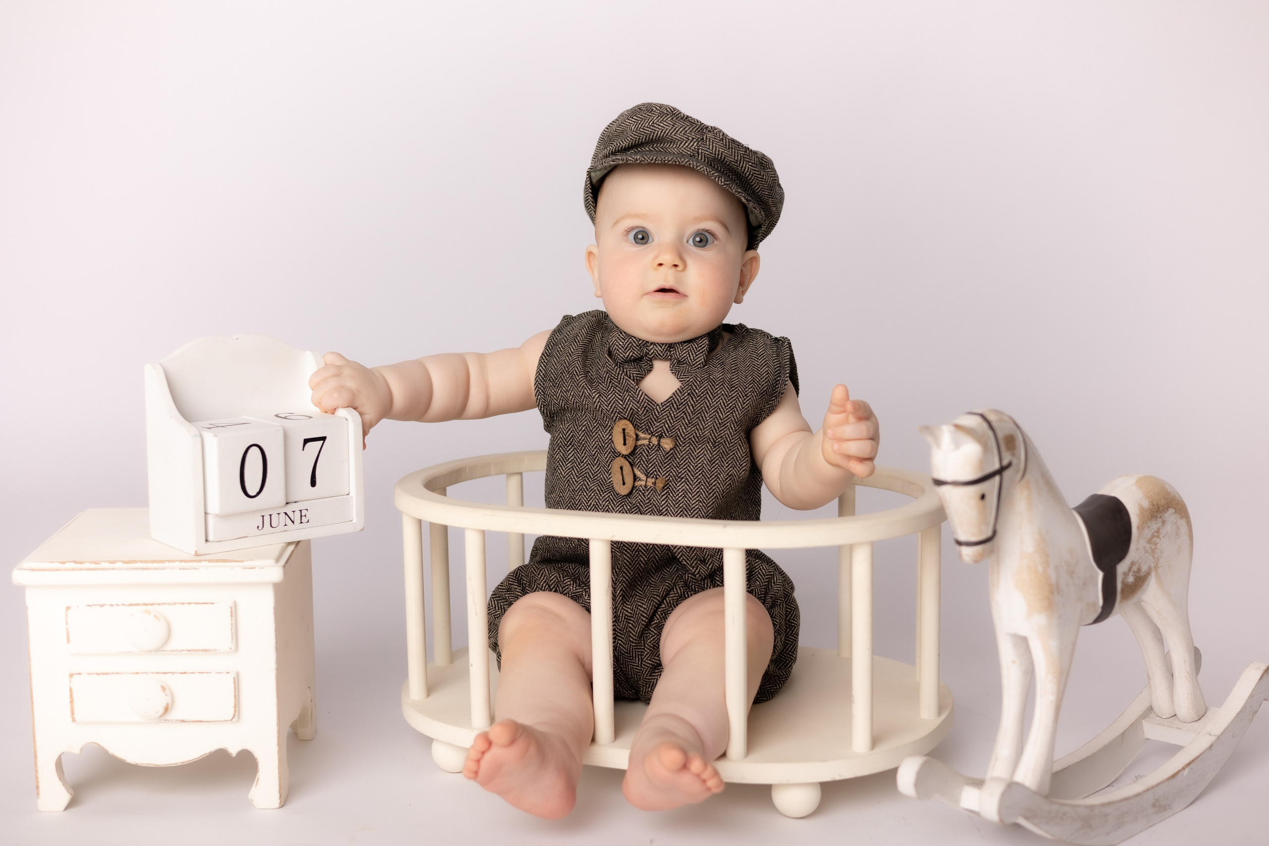 Младенец в ретро одежде сидит на детском стульчике с буквенными кубиками и игрушечной лошадью.