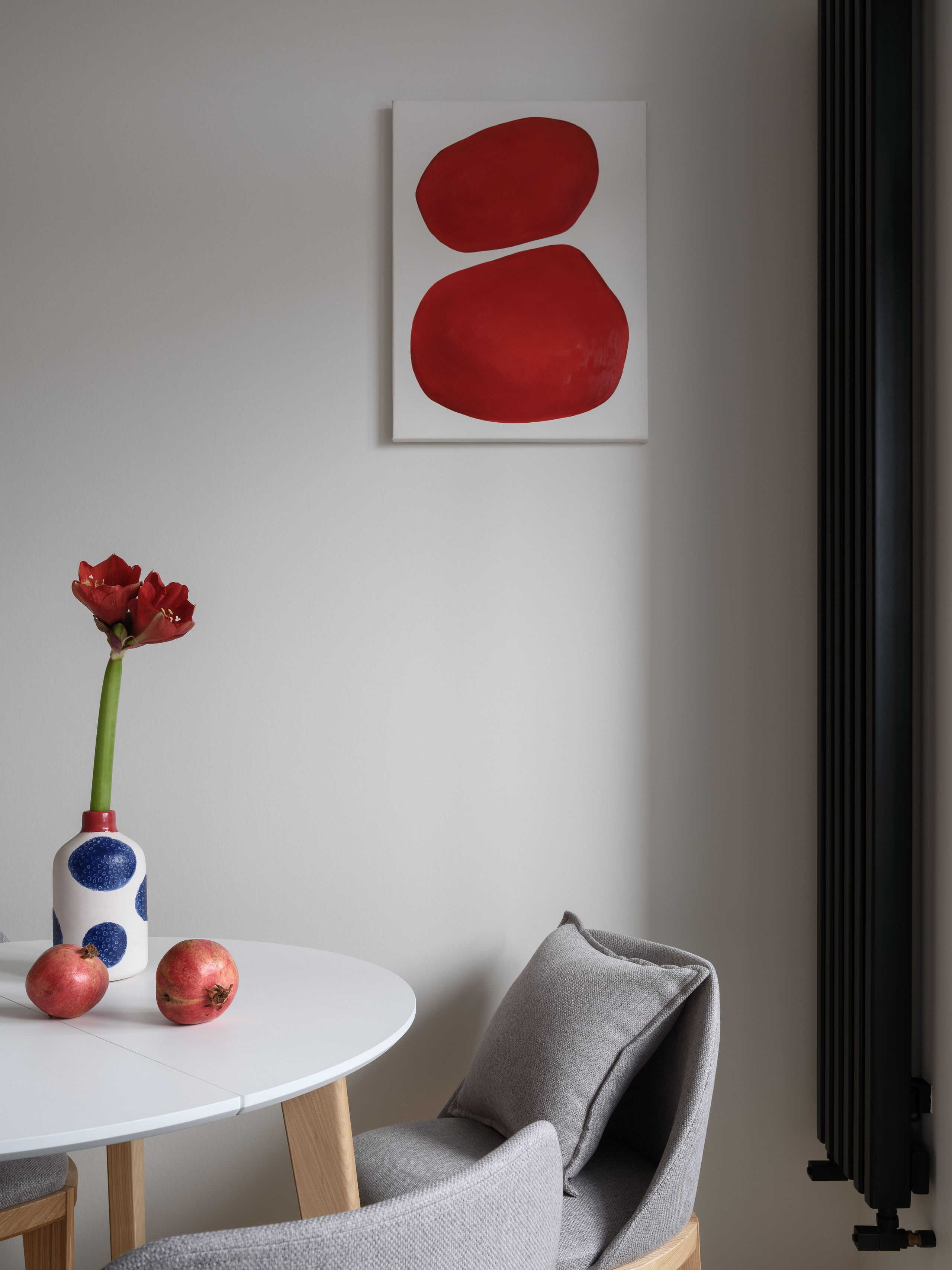 Современный обеденный уголок: белый круглый стол, серые дизайнерские стулья и абстрактная картина с красными акцентами. Автор проекта — Евгения Княжева и Владлена Привалова, фотограф Сергей Денисенко