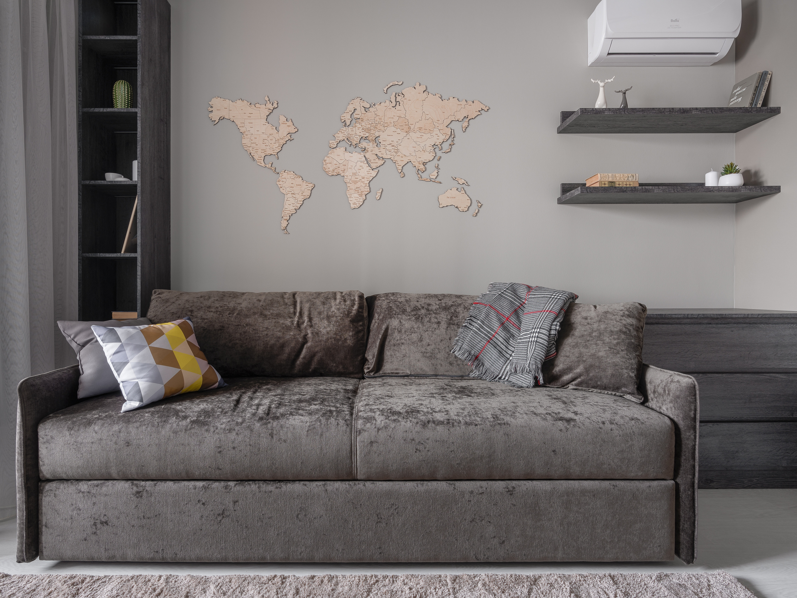 Интерьер гостиной с мягким серым диваном, декоративной картой мира на стене, открытыми полками и акцентными подушками, дизайн Алина Ляхова, интерьерная фотография Сергей Денисенко.