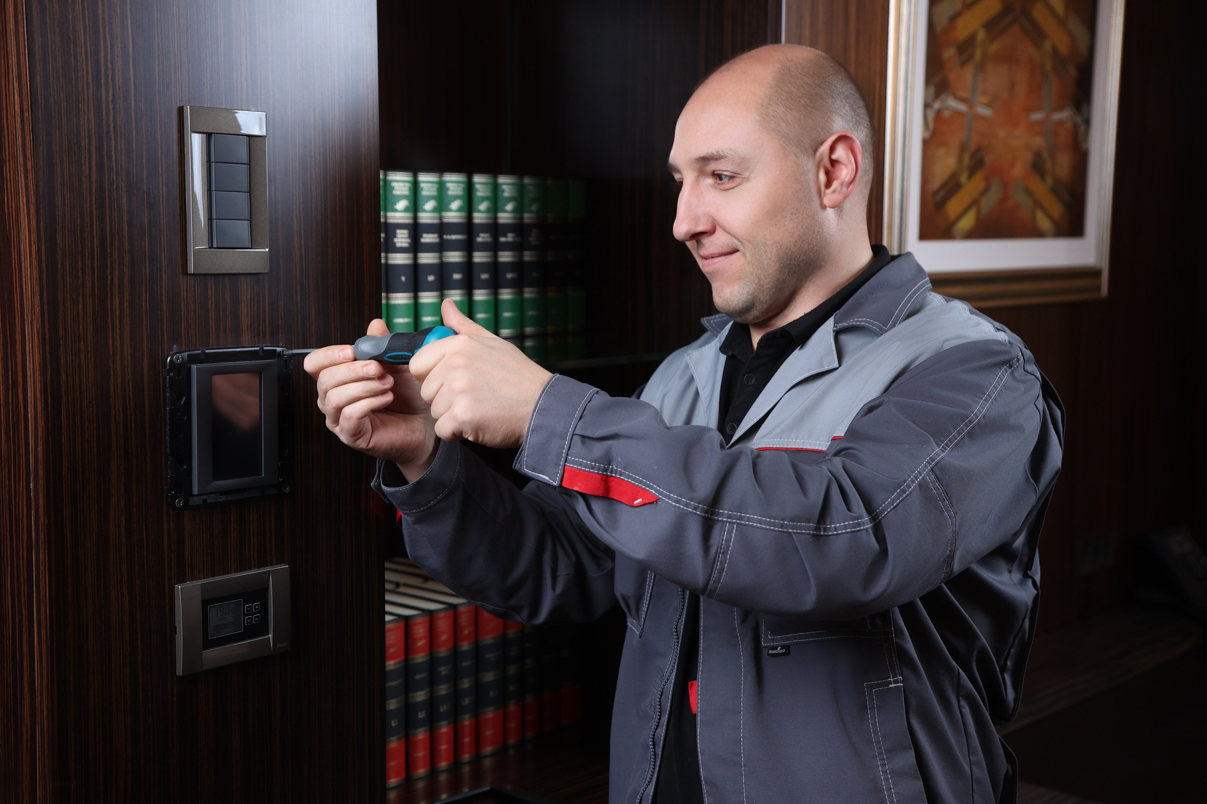 Техник службы эксплуатации отеля выполняет мелкий ремонт розетки в гостевом номере. Фото рабочего процесса.