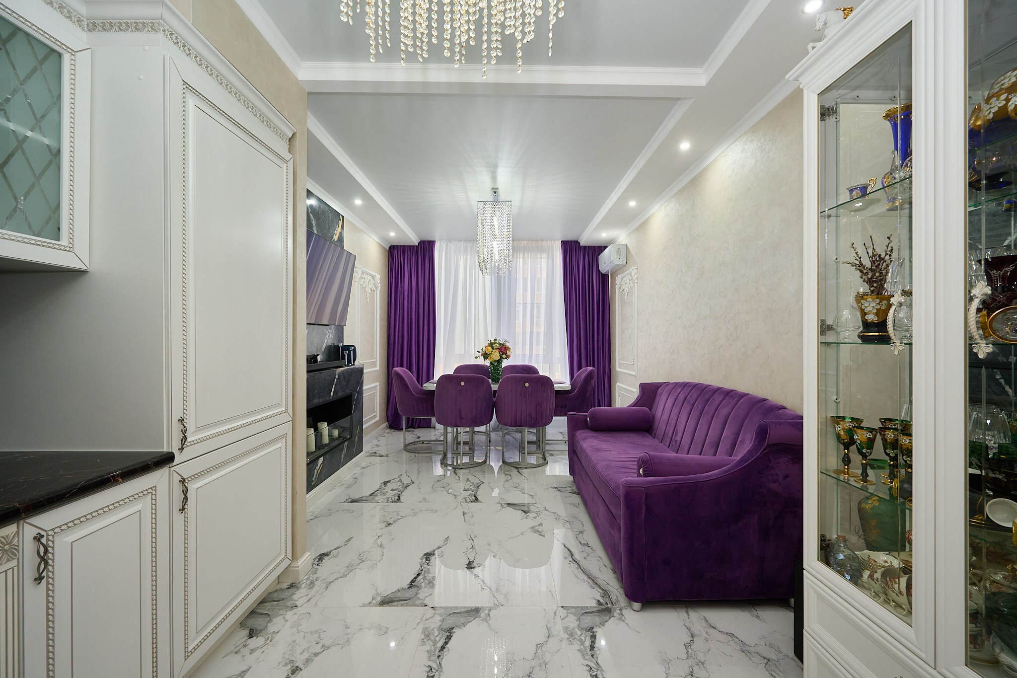 светлые плиты фиолетовый диван фиолетовые шторы белый стол фиолетовые стулья белый стеклянный буфет телевизор 