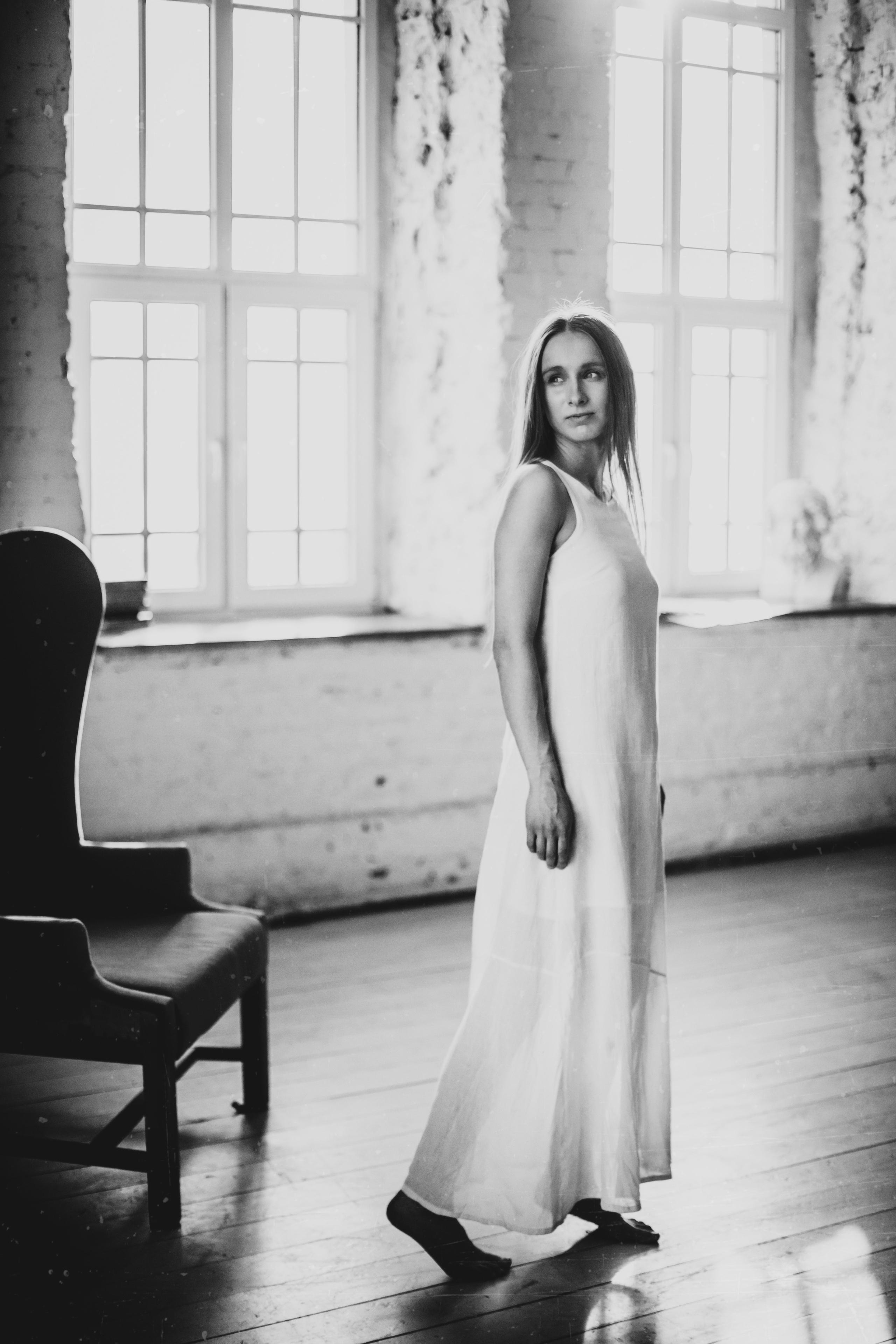 студийный портрет женщины в длинном белом платье на фоне белого кирпича