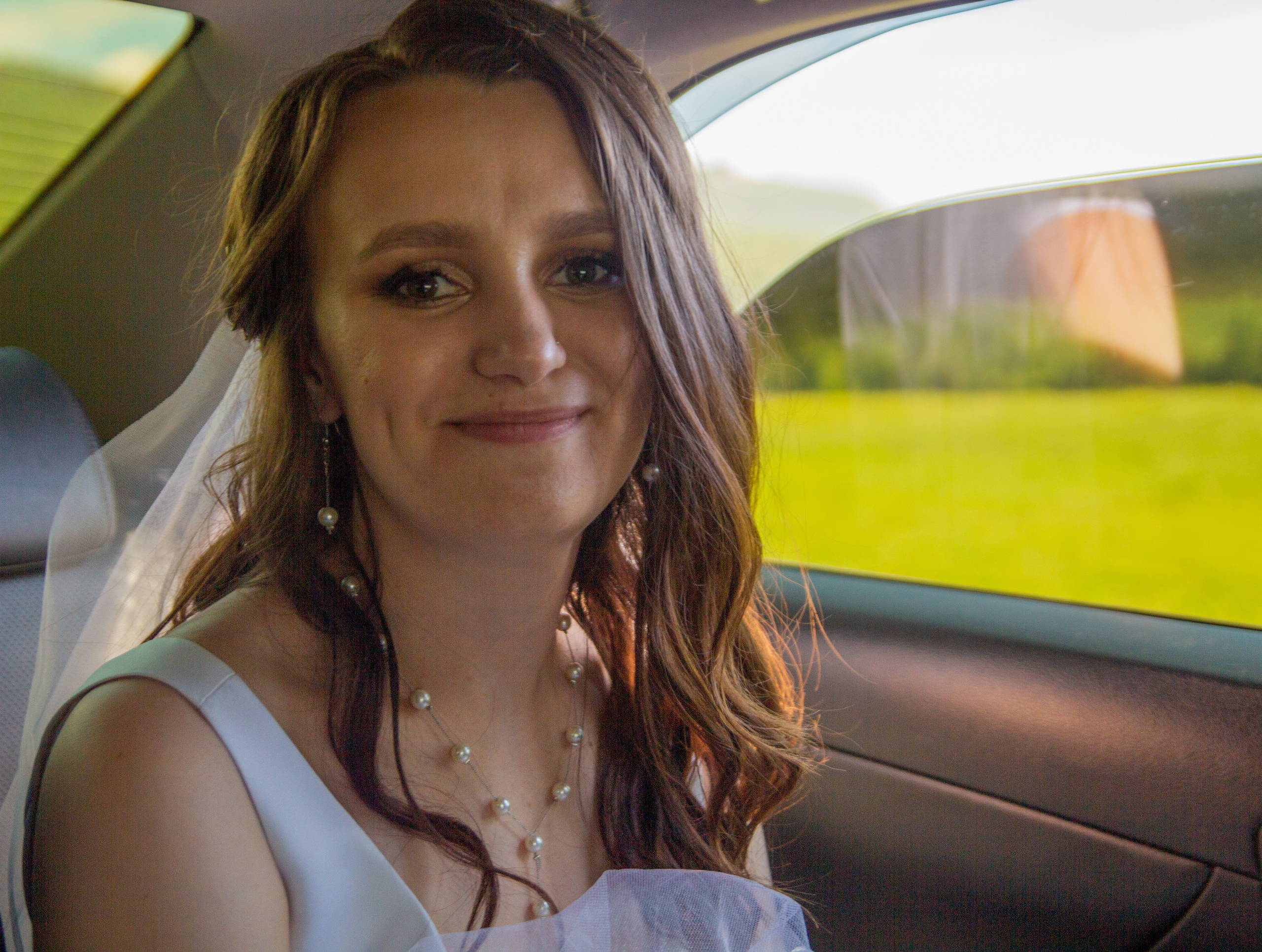 Портрет невесты в машине, с фатой и нежной улыбкой — ожидание церемонии или отдыха.