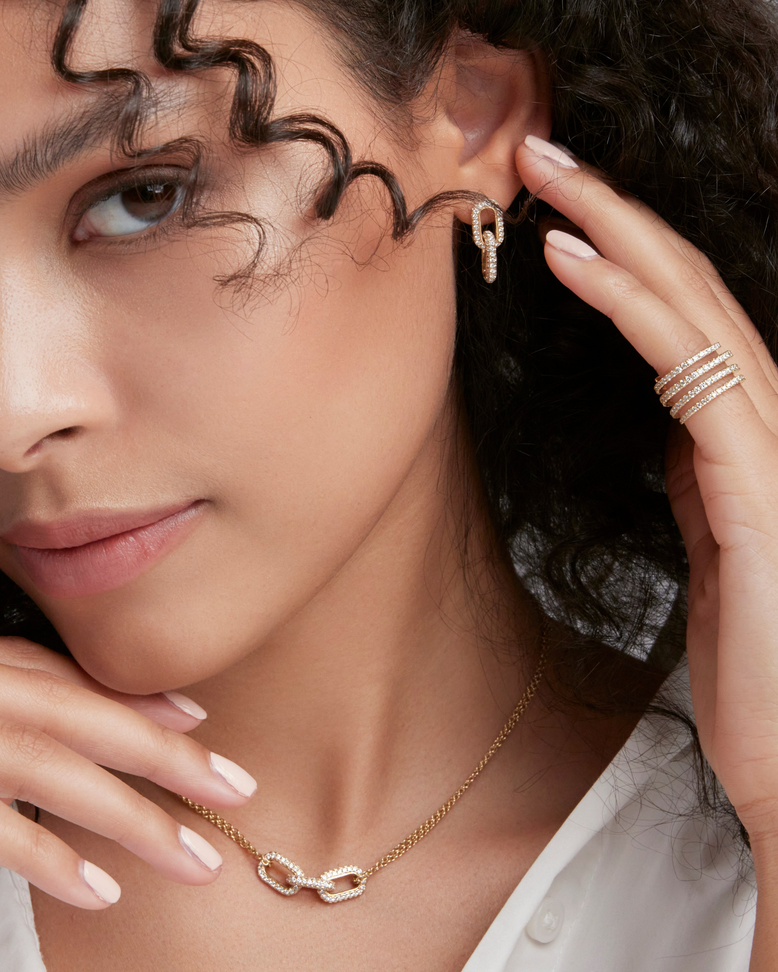Model touching her earring with a soft expression, showcasing fine jewelry details.