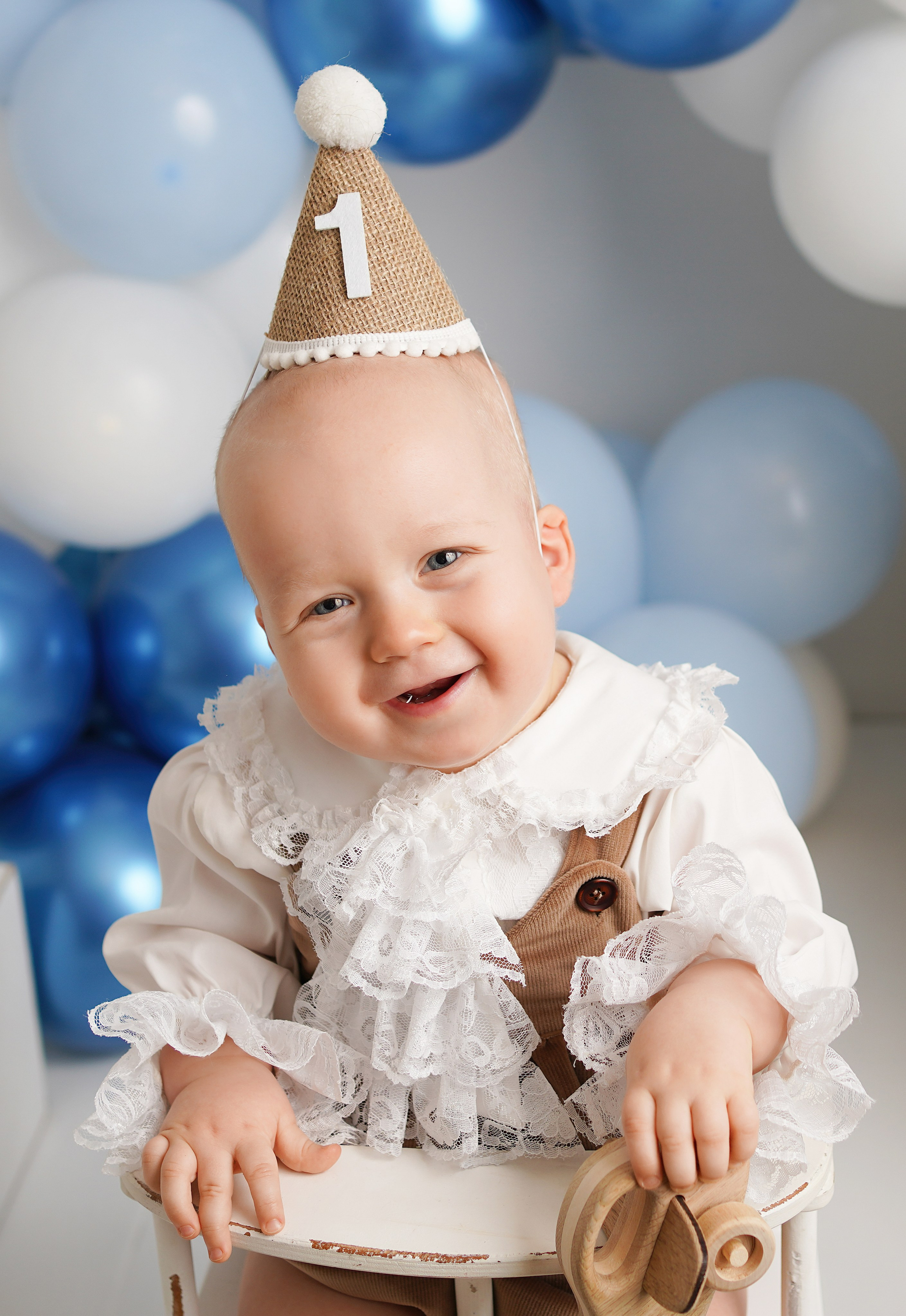 На фото улыбающийся малыш в нарядной одежде и колпачке .