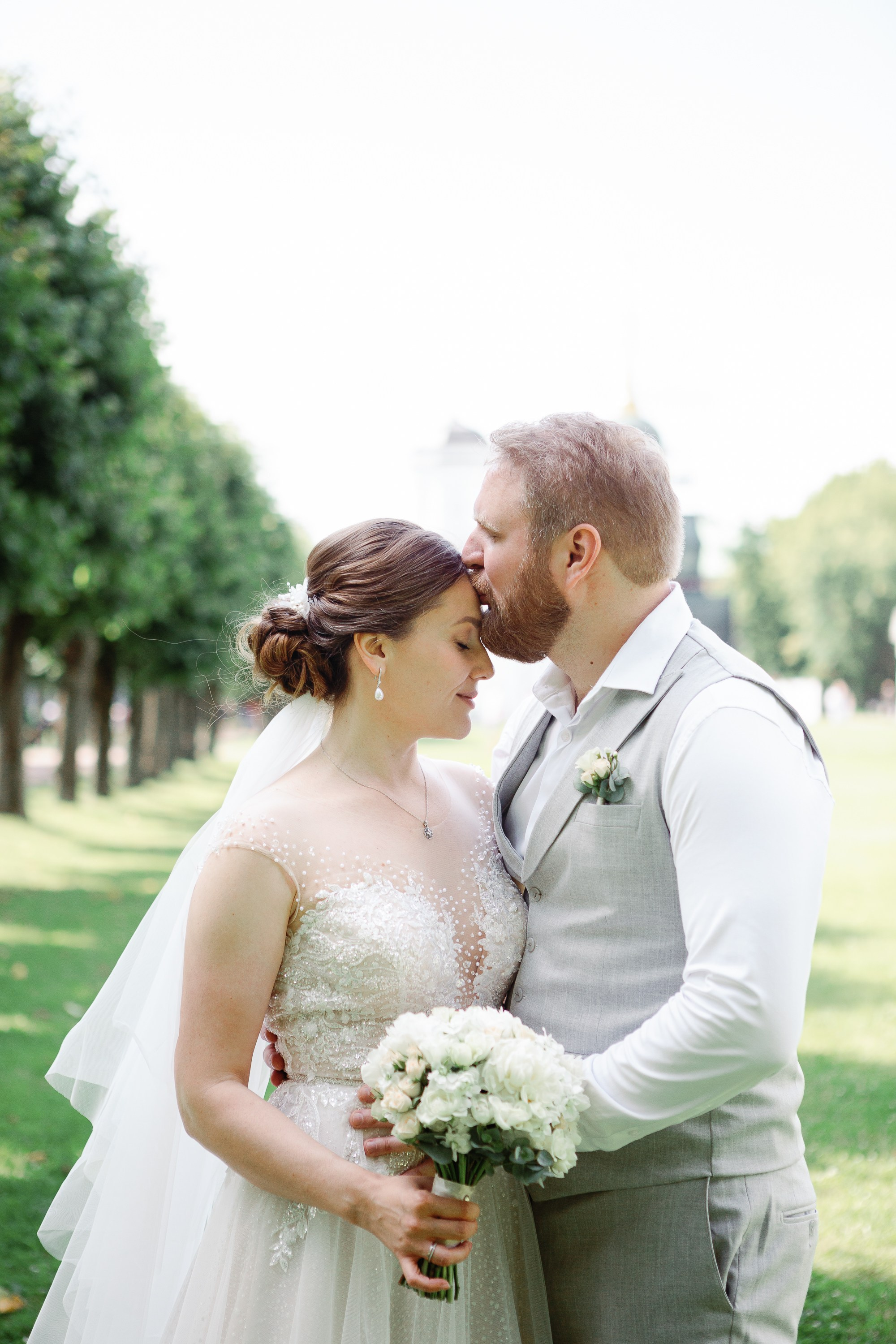 Жених обнимает и целует невесту в парке в Москве.