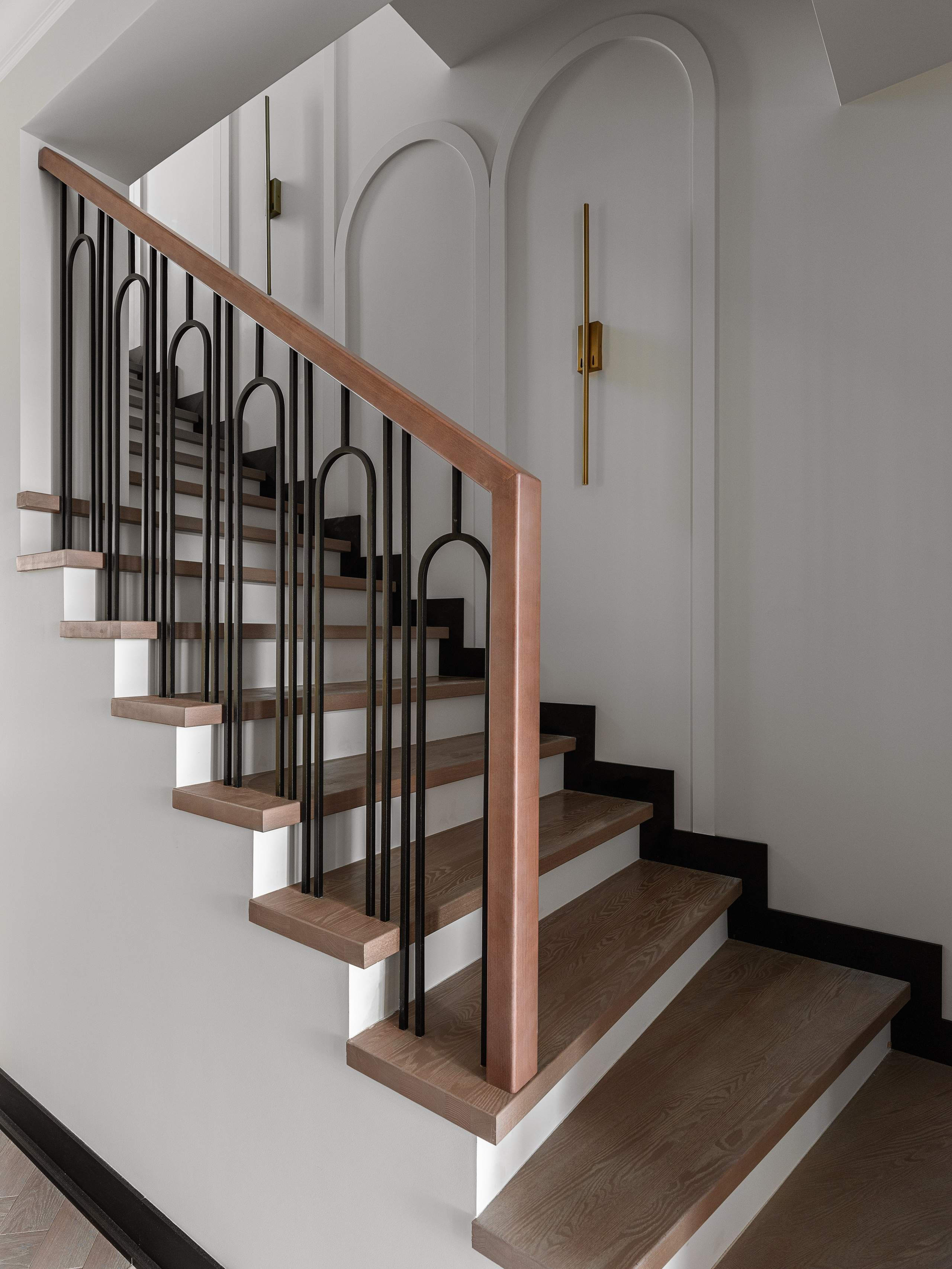 Стильная современная лестница с деревянными ступенями и черными металлическими перилами в интерьере частного дома. Элегантные арочные панели и латунные бра подчеркивают дизайн Василиссы Бачевой, стилистика Натальи Якушевой, фото Сергея Денисенко.