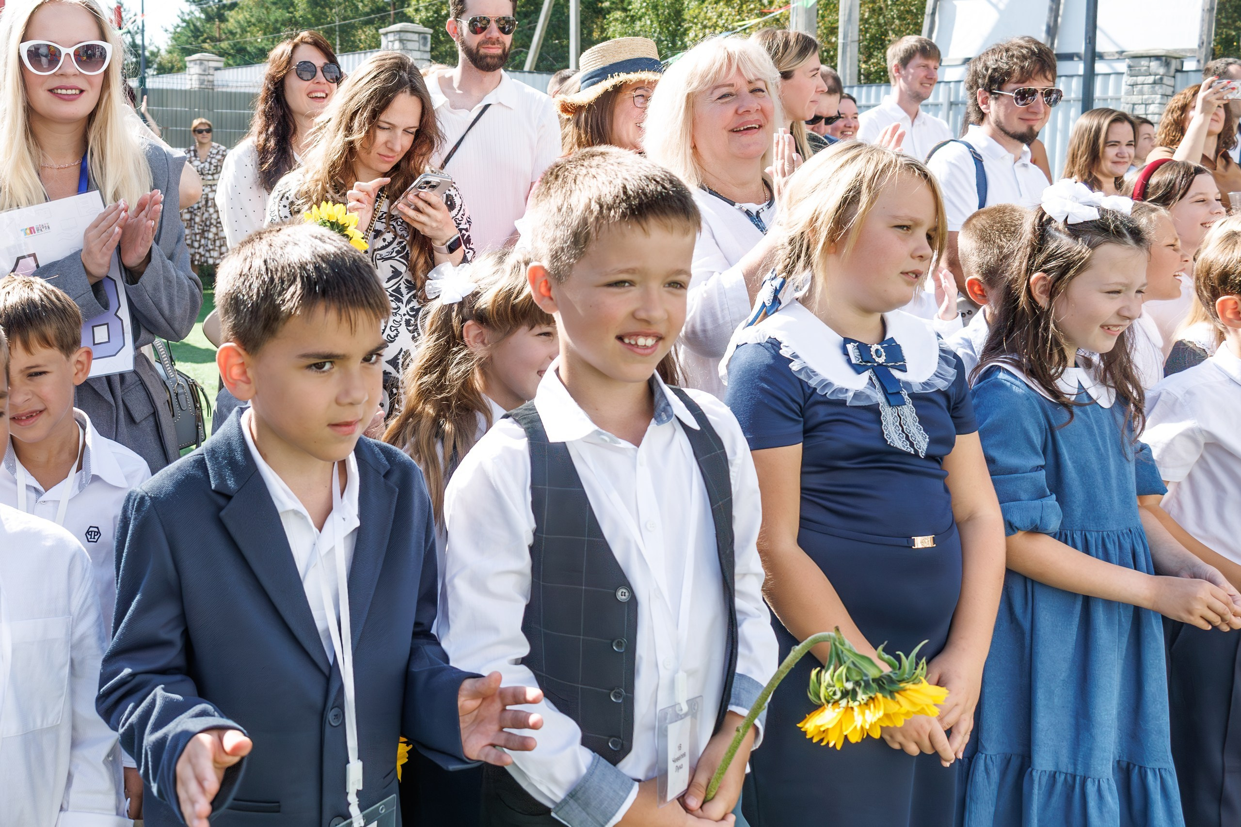 Линейка 1 сентября в школе - дети с букетами, радостные родители и учителя; дети обнимаются, радуются встрече с друзьями после каникул