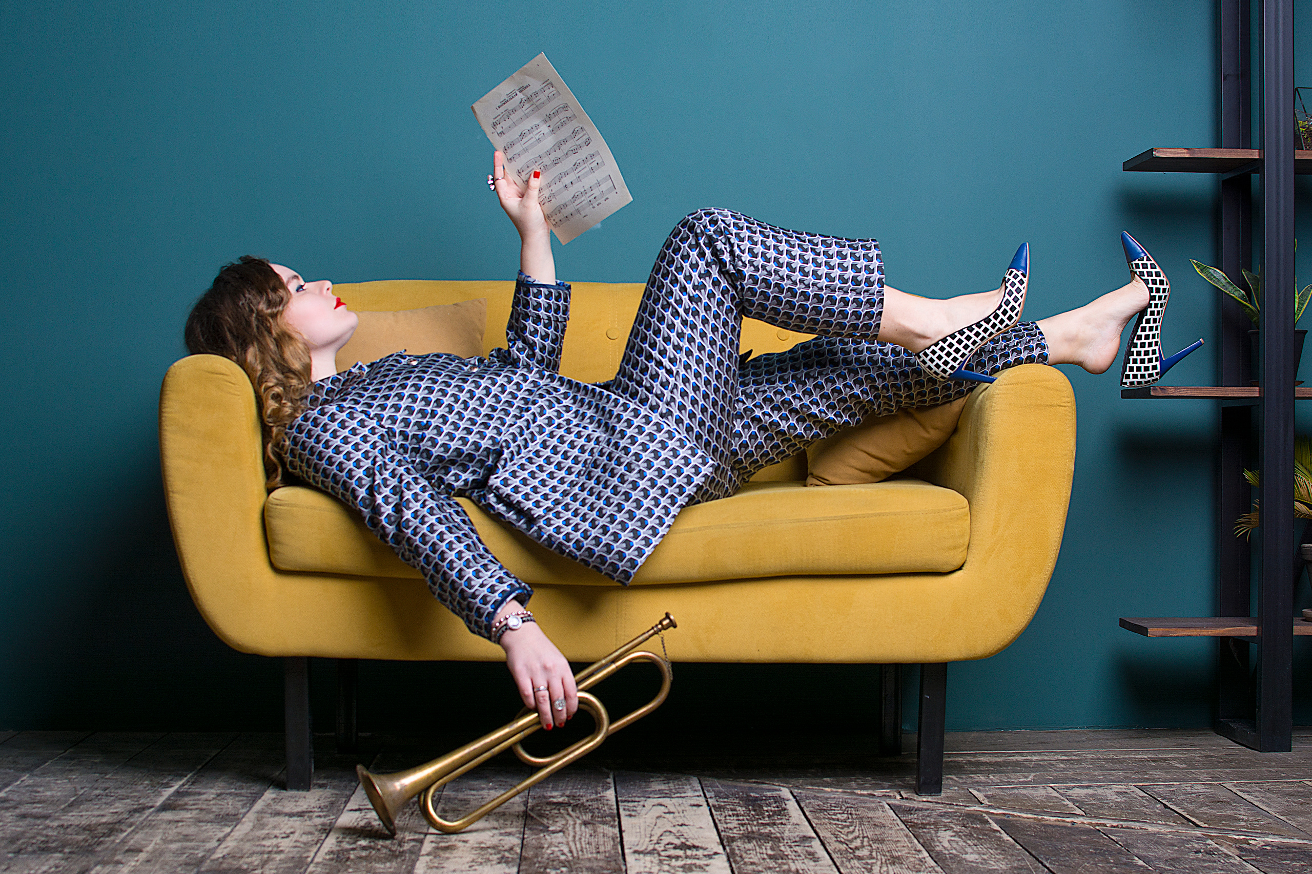 девушка в клетчатом костюме с трубой и нотами на желтом диване 