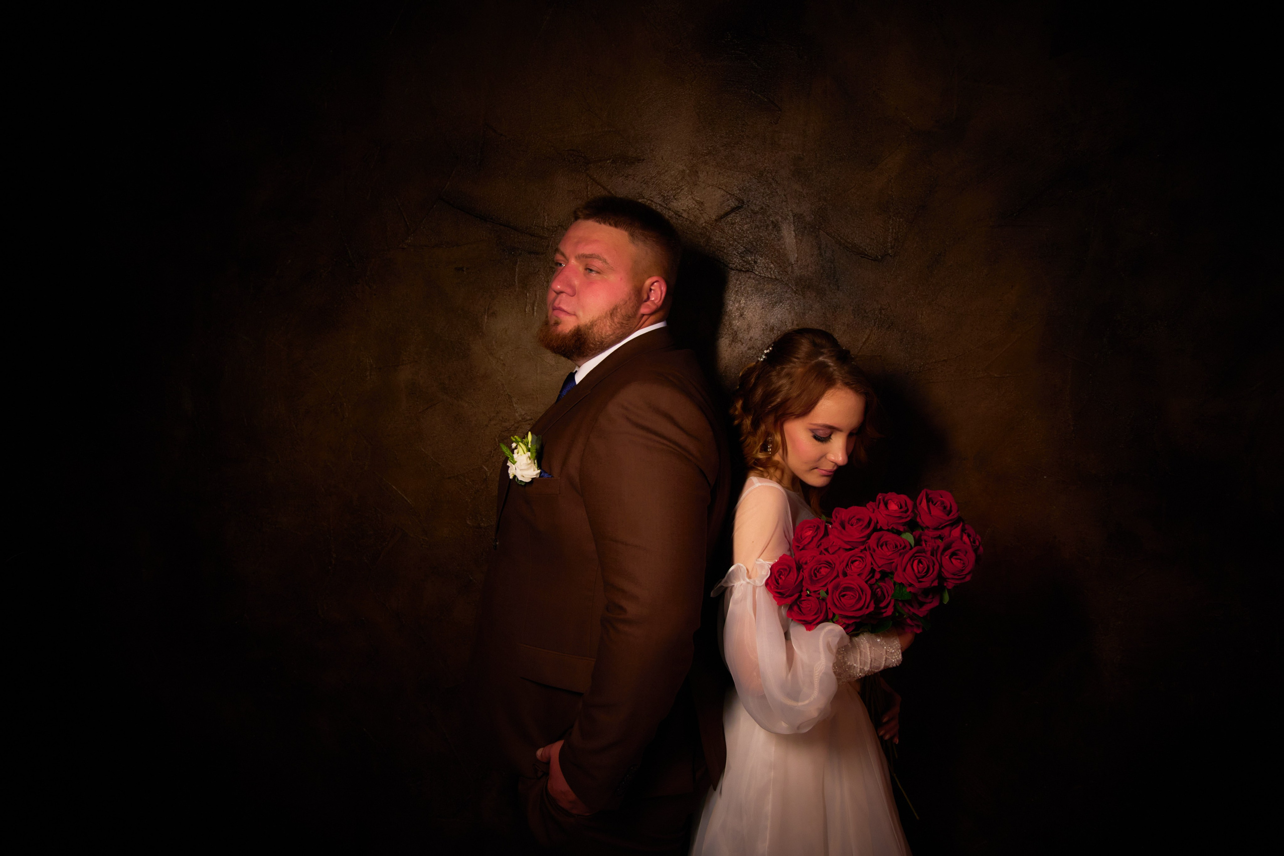 невеста нюхает красные розы, а за спиной стоит влюбленный жених