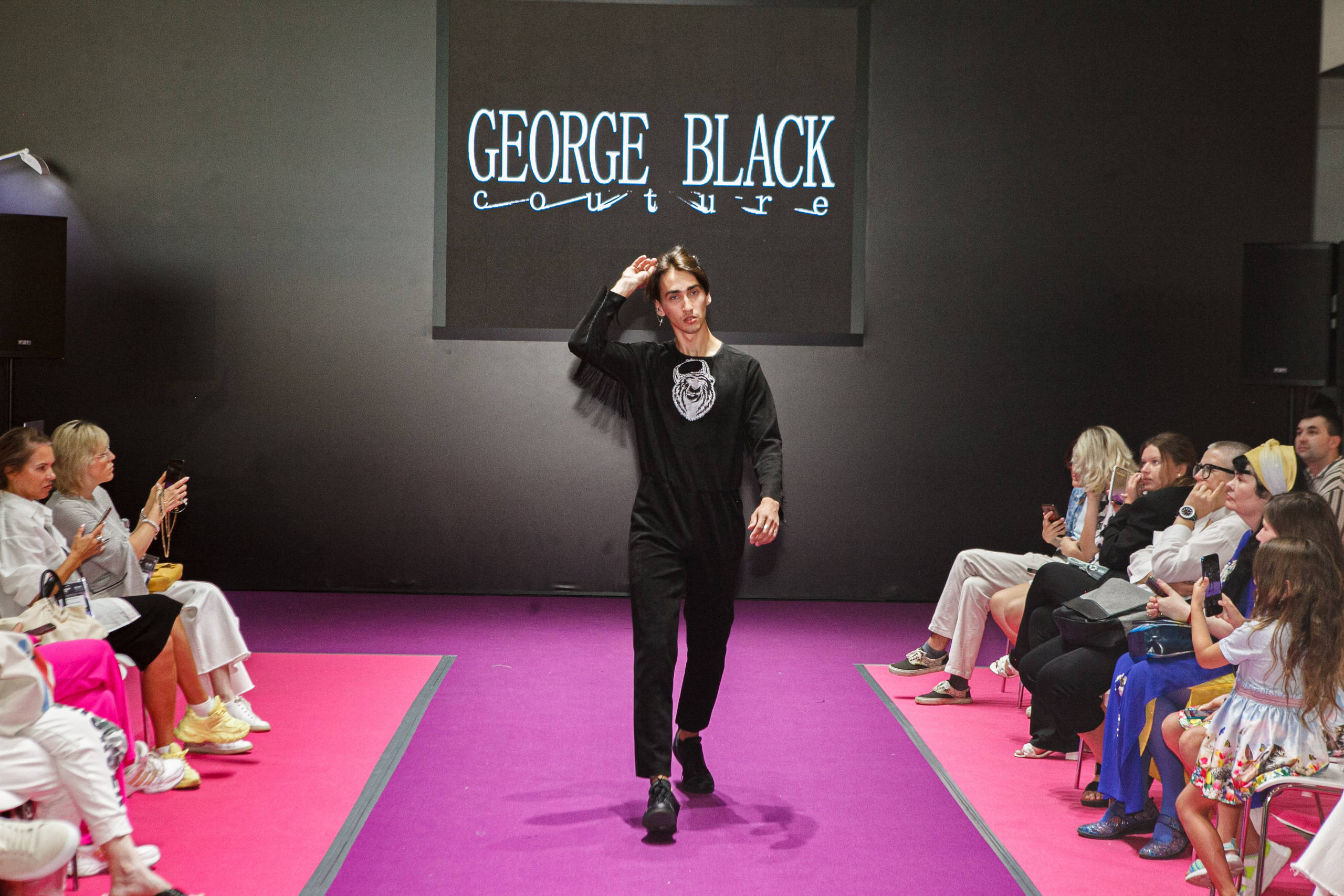  "Модели в ярких нарядах проходят по подиуму во время показа мод, освещенные яркими софитами и окруженные восторженными зрителями."