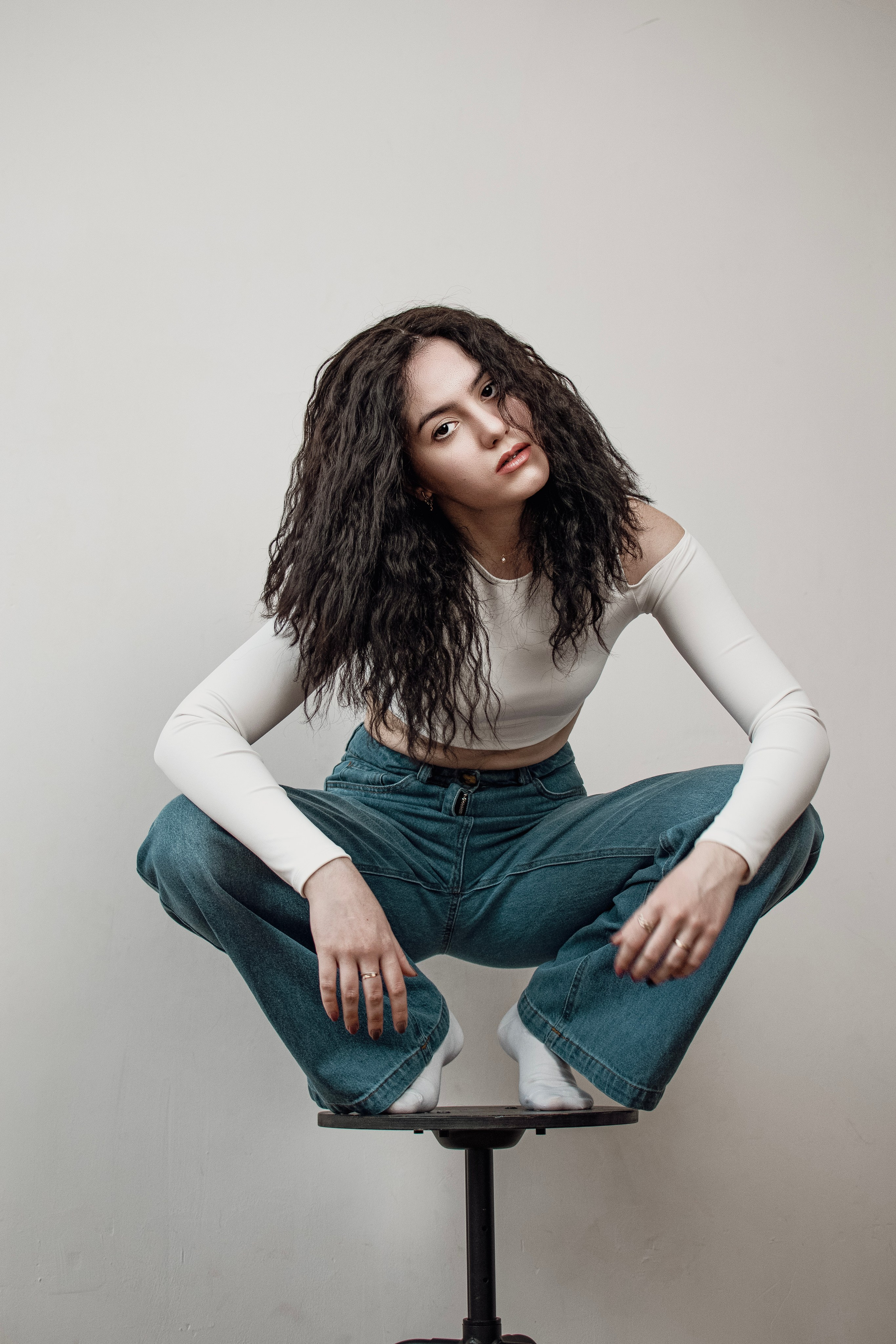 Кучерявая брюнетка на корточках сидит на стуле