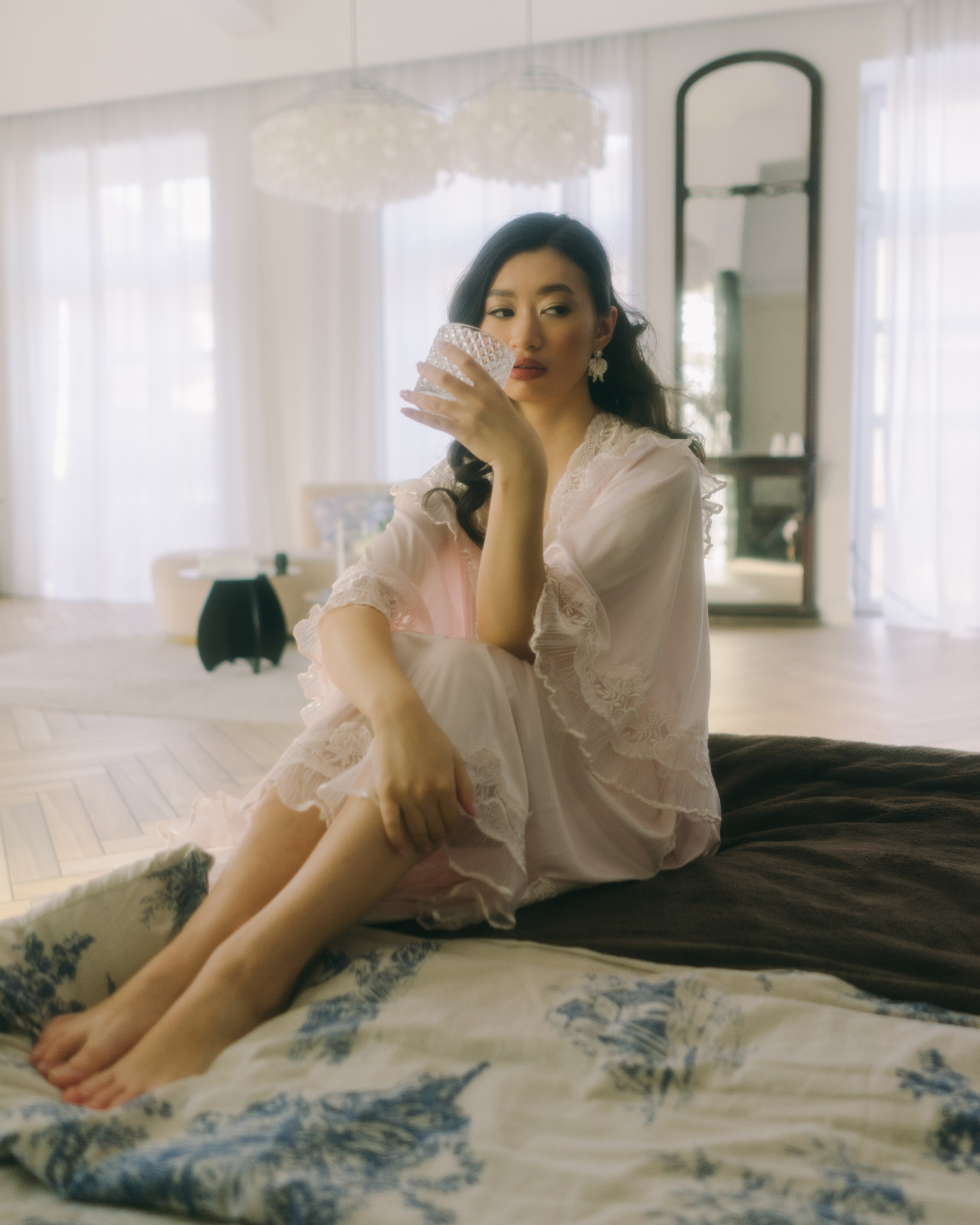 Невеста сидит на кровати с бокалом, эстетичная bridal boudoir фотосессия в киношном стиле