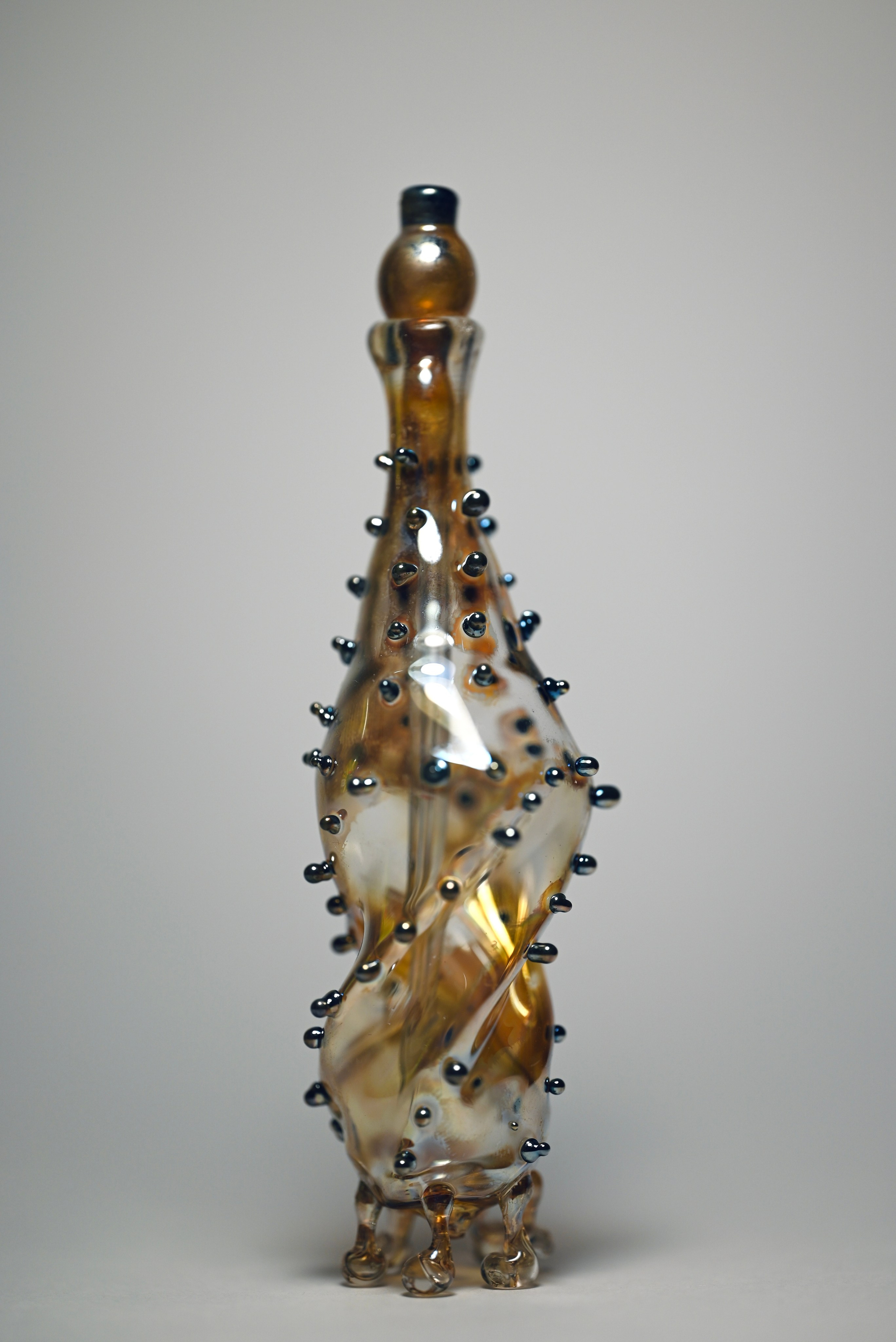 alt="Авторская стеклянная скульптура с прозрачной крышкой, янтарным корпусом и декоративными каплями на поверхности."