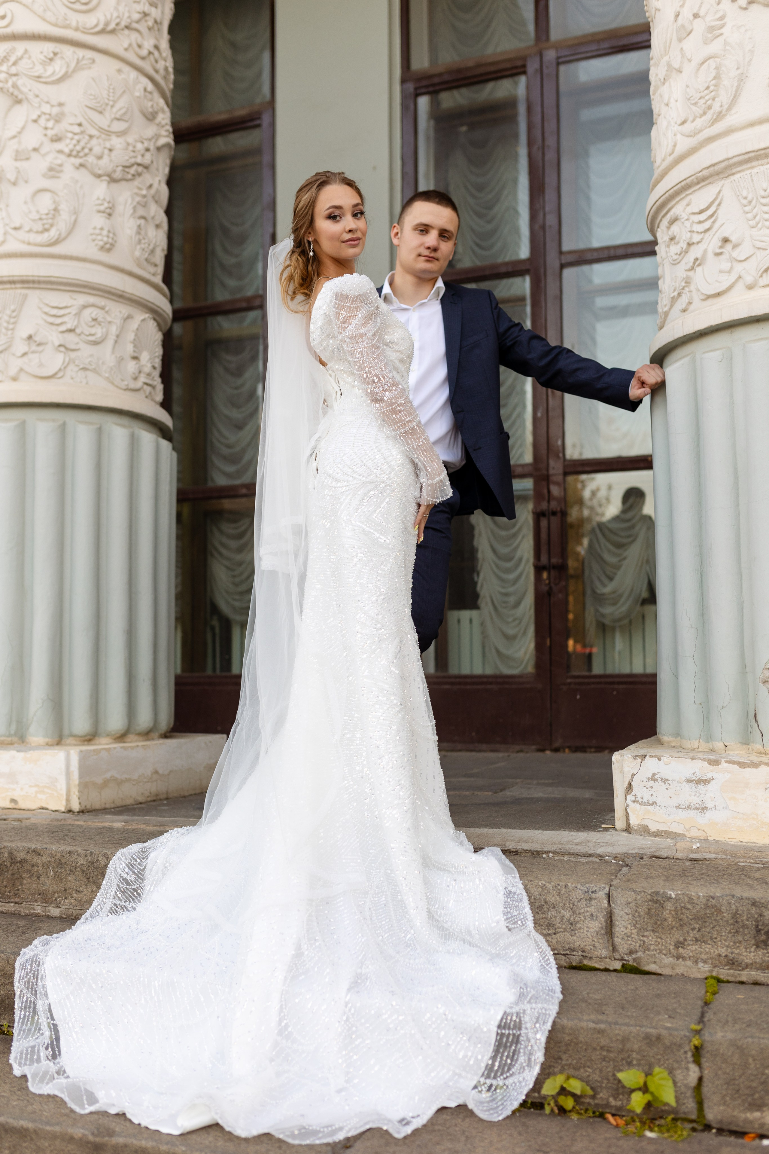 молодые стоят у здания, по ступенькам струится  шлейф платья невесты.