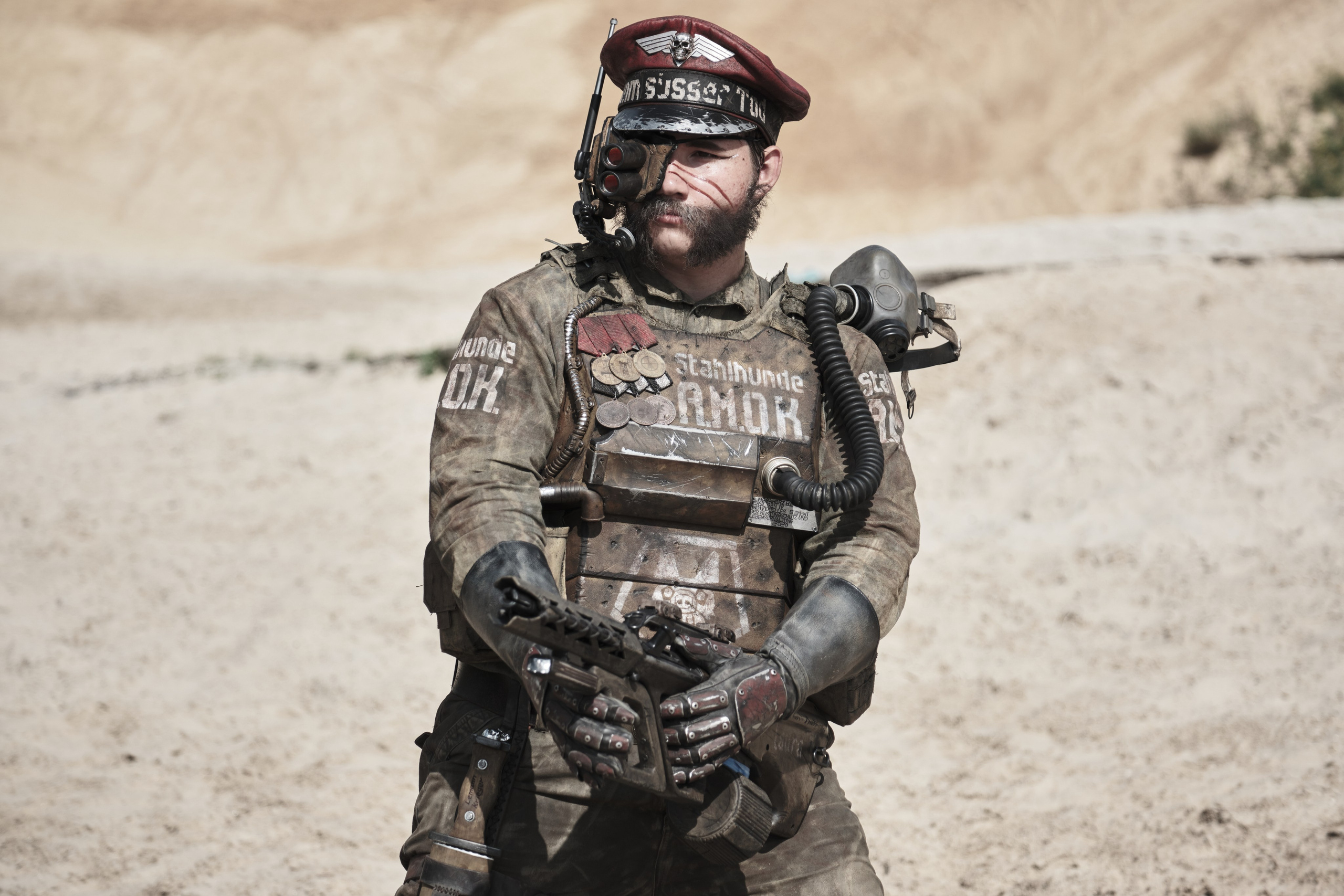 Мужчина в боевом костюме целиться из автомата в стиле пост апокалипсис