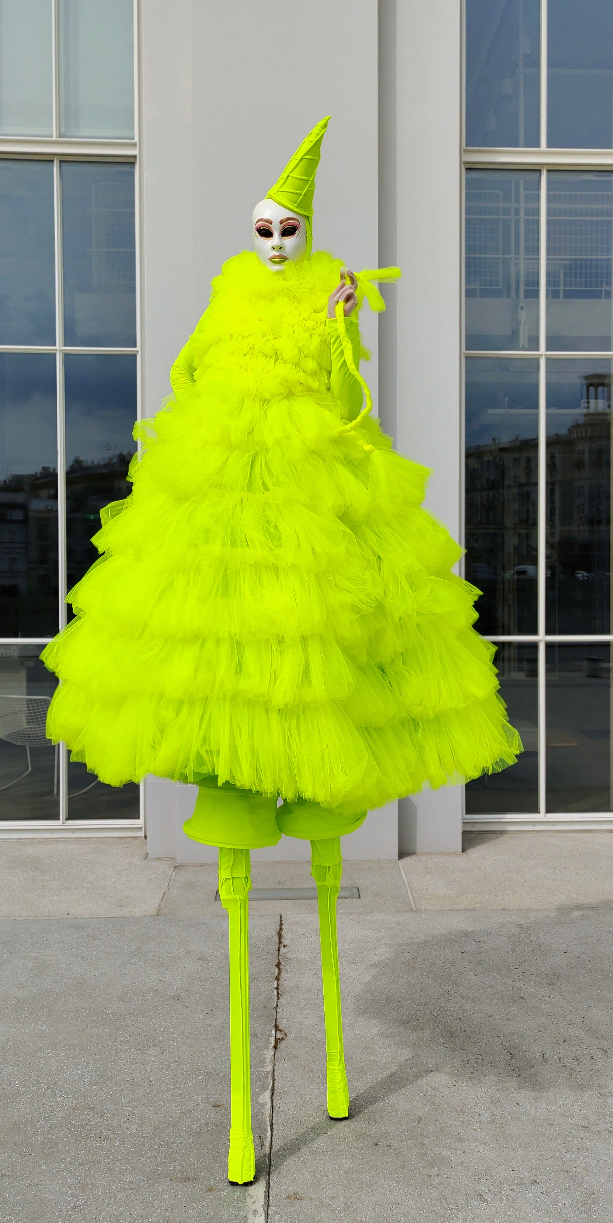 Ходулист позирует гостям мероприятия и фотографу у ресторана с большими окнами