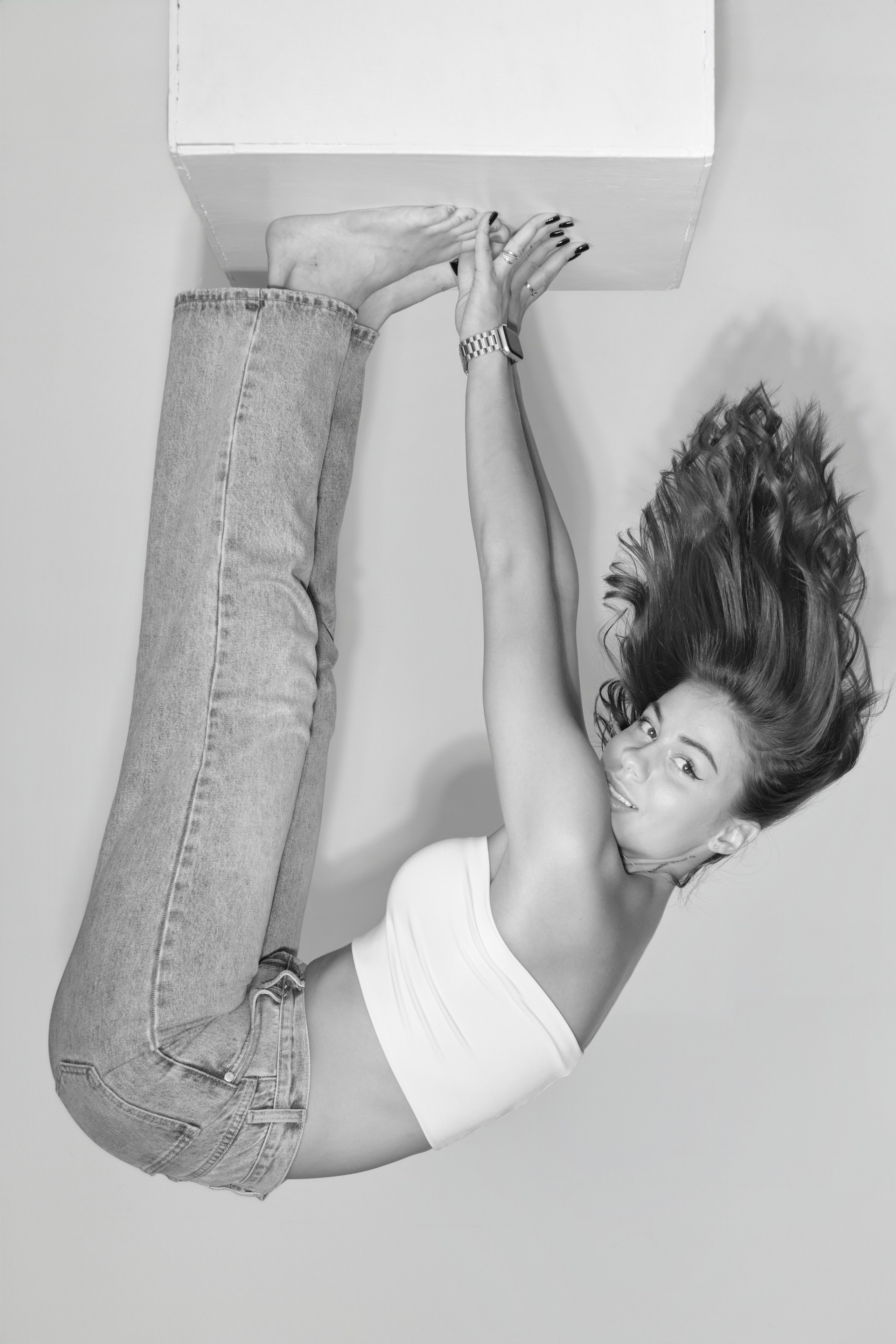 Черно-белая фотография: девушка-модель лежит на полу, закинув ноги на белый куб. Креативное позирование для тестов.