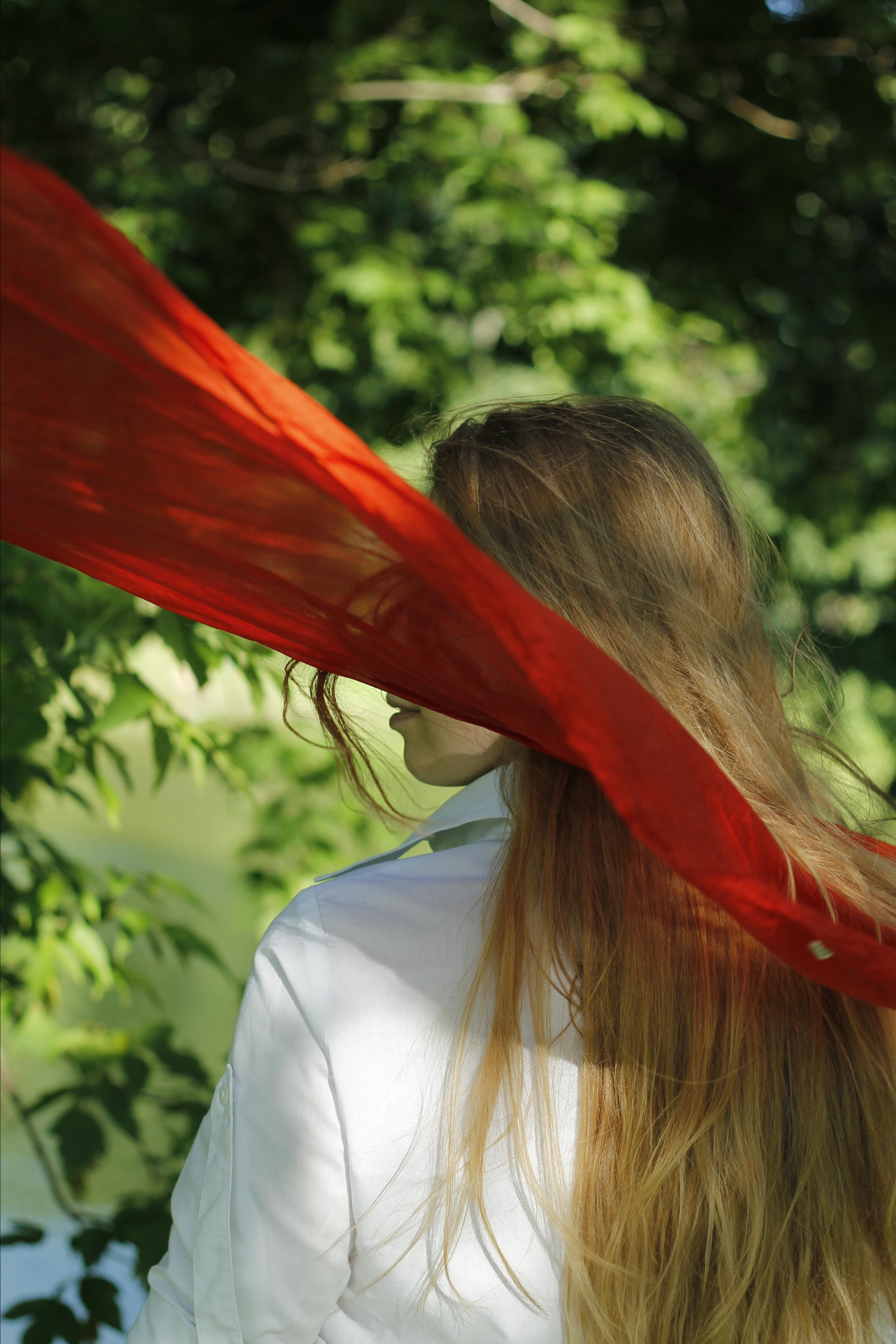 Photo of woman with a red flying scarf and  whit a tree on background by Anna Karamurzina