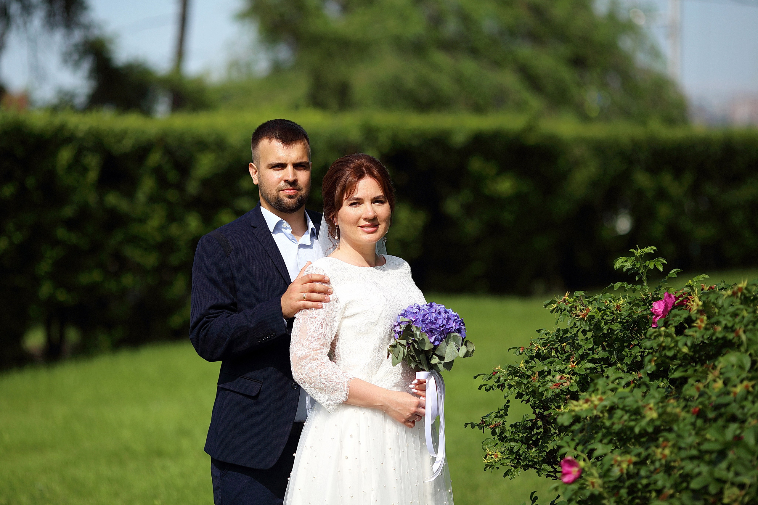 Жених держит невесту за плечи, нежная фотография в зелени