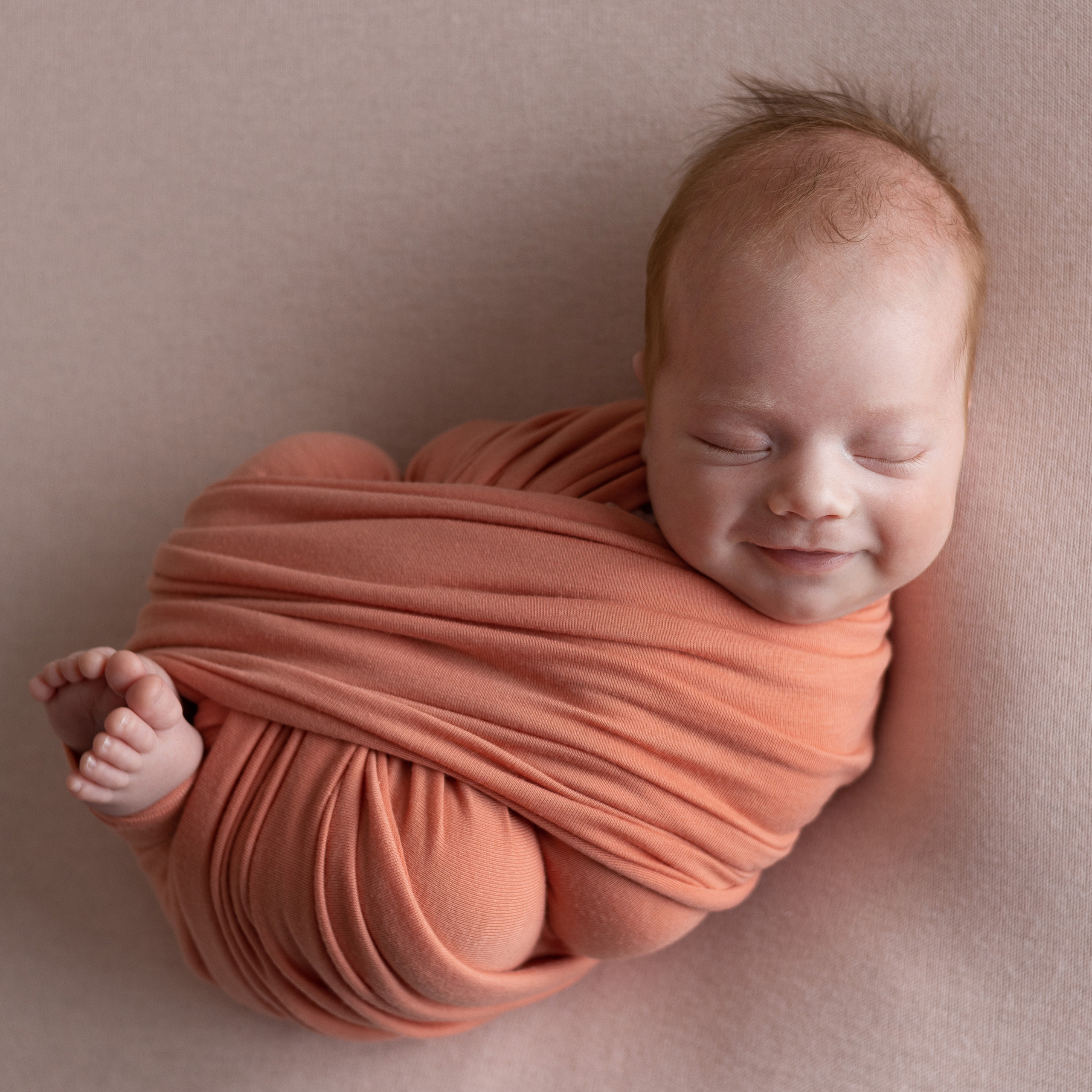 улыбается девочка в розовой обмотке на розовом фоне