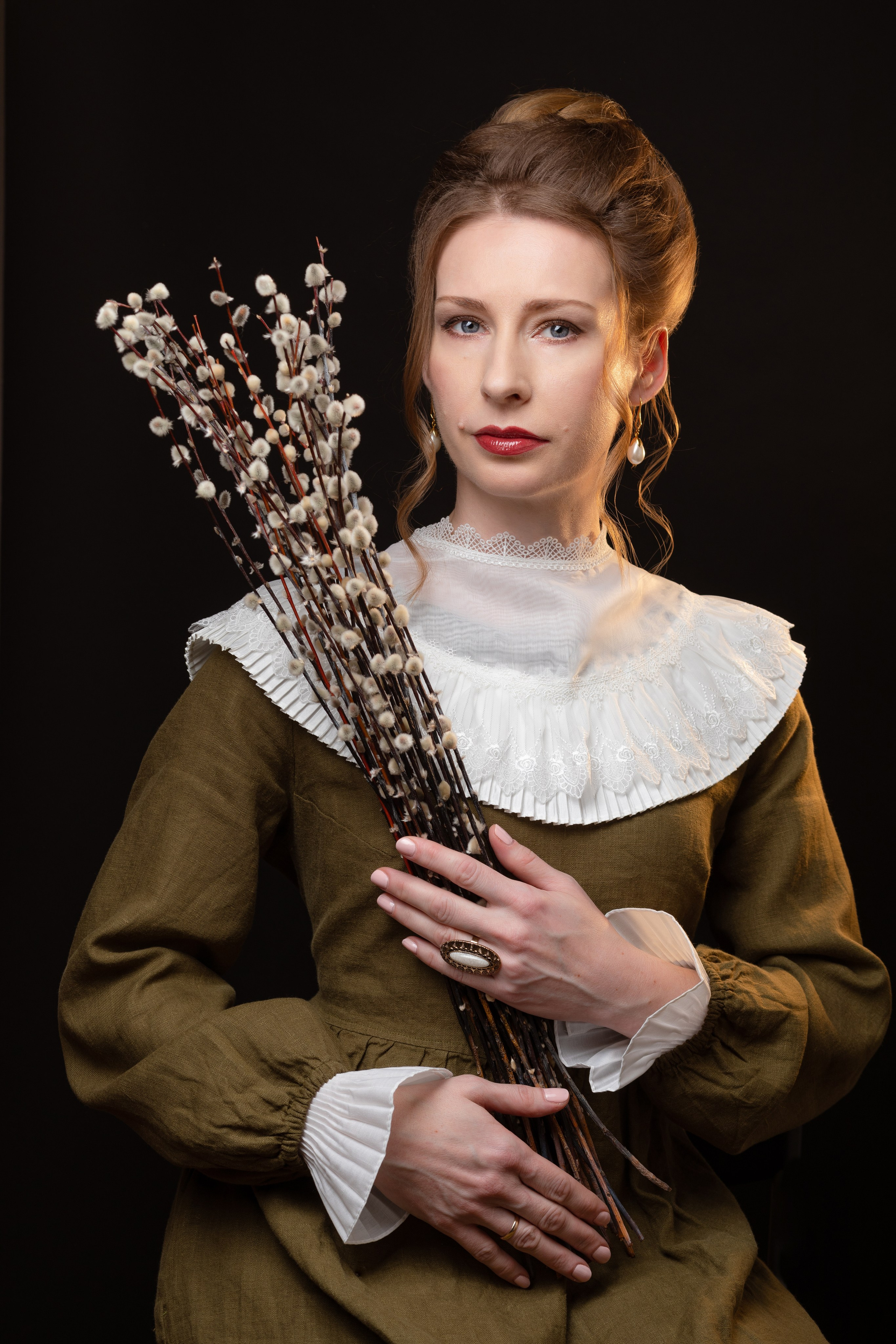 девушка сидит на стуле одета в зелёное льняное платье и держит букет вербы