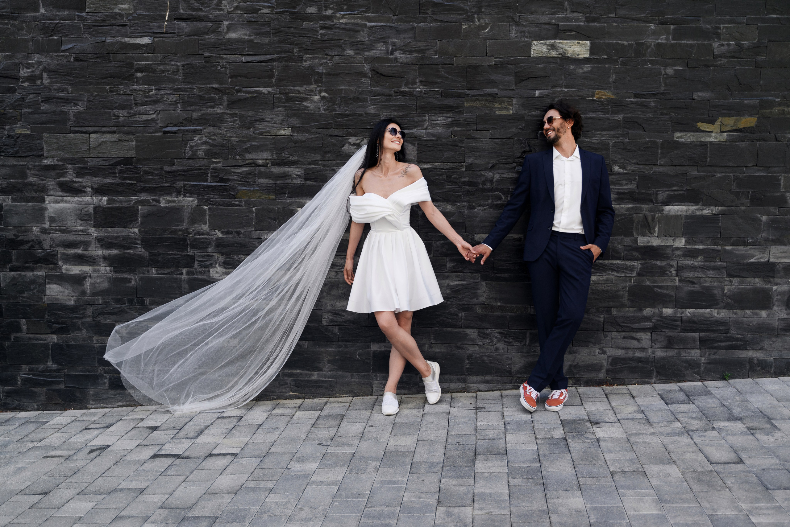 Молодые стоят у стены взявшись за руки и смотрят друг на друга 