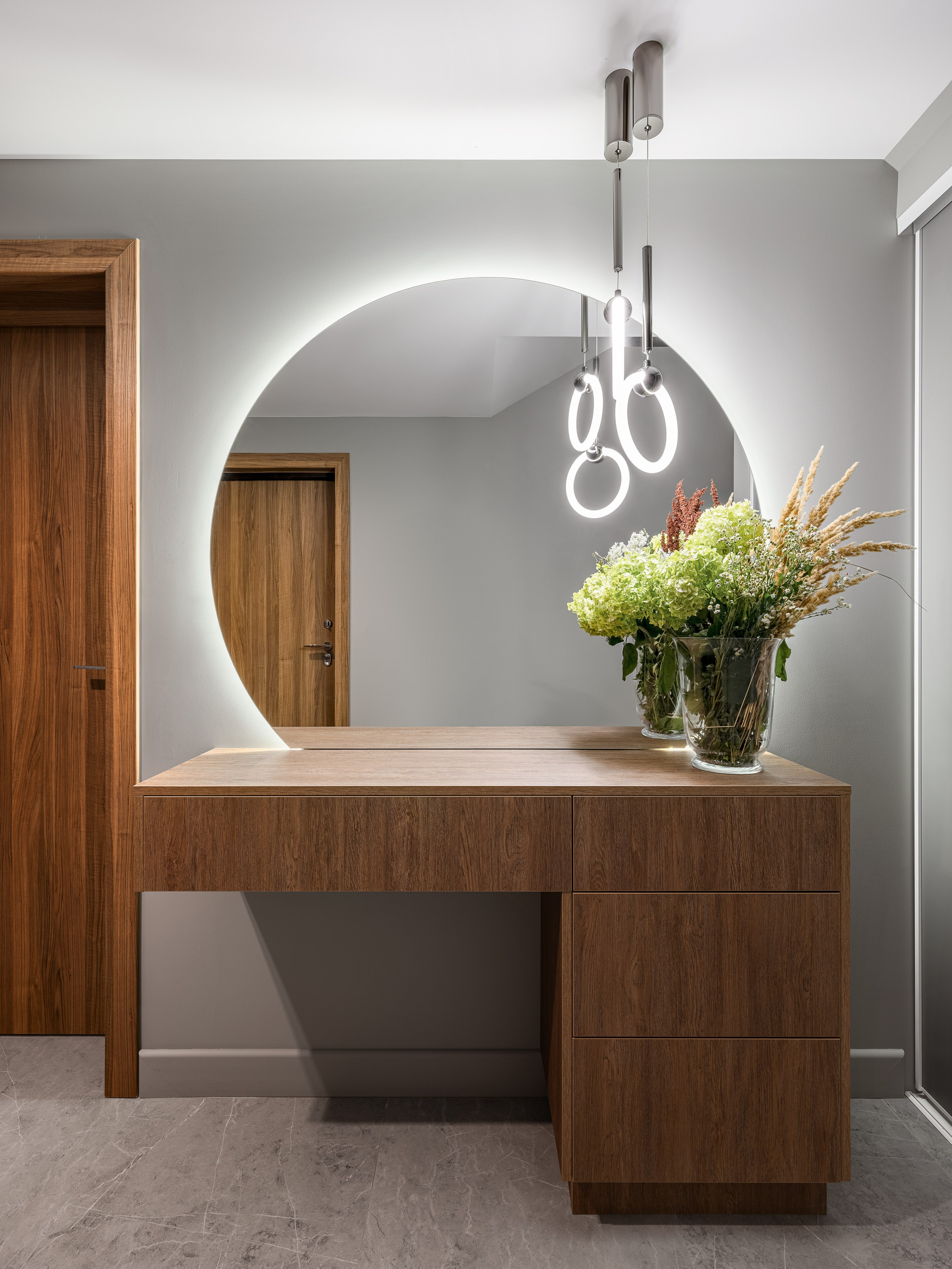 Стильная прихожая с круглым зеркалом с подсветкой, деревянной консолью и букетом цветов в стеклянной вазе, дизайнеры интерьера Алёна Попова и Анастасия Дмитриева, фотограф Сергей Денисенко, современный минимализм с элементами дерева.