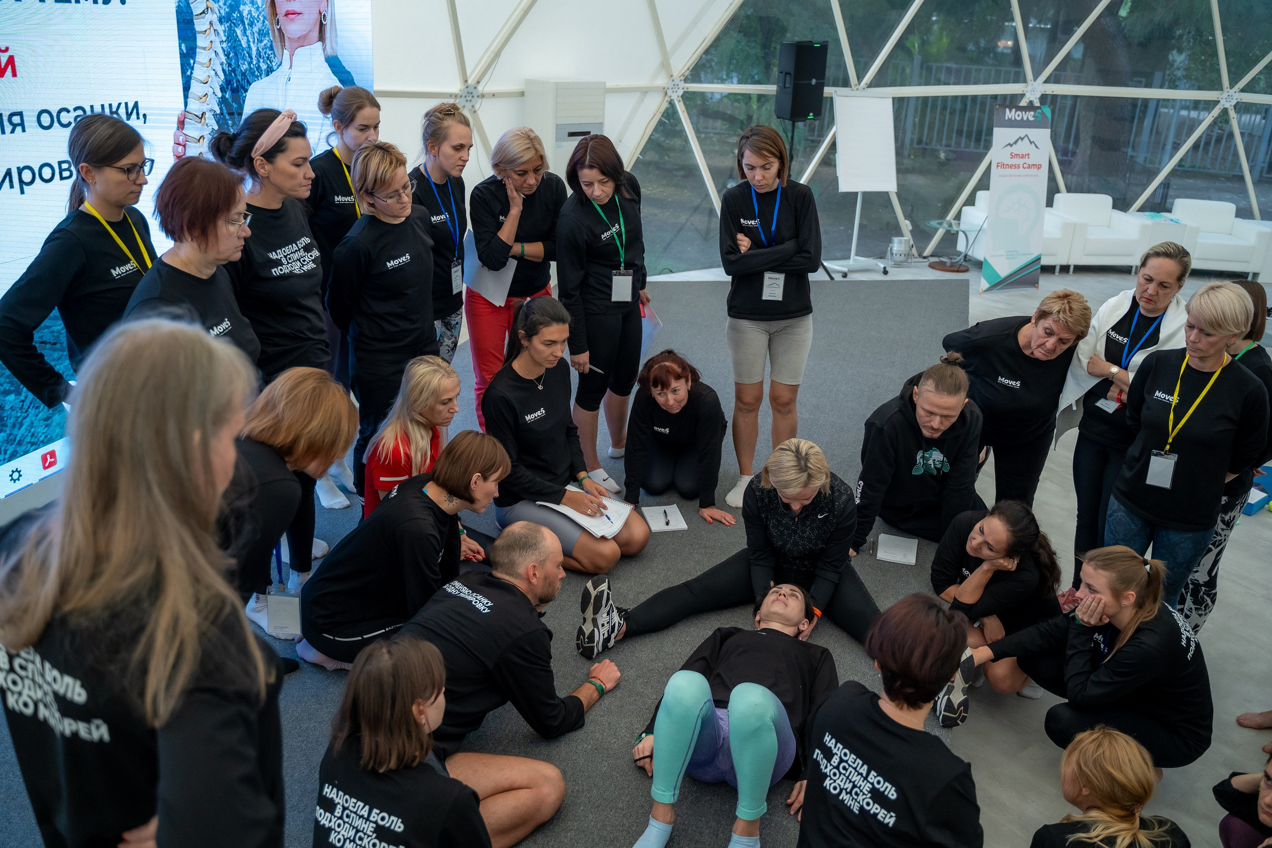 Тренер  фитнес концеренции показывает упражнение на примере участницы