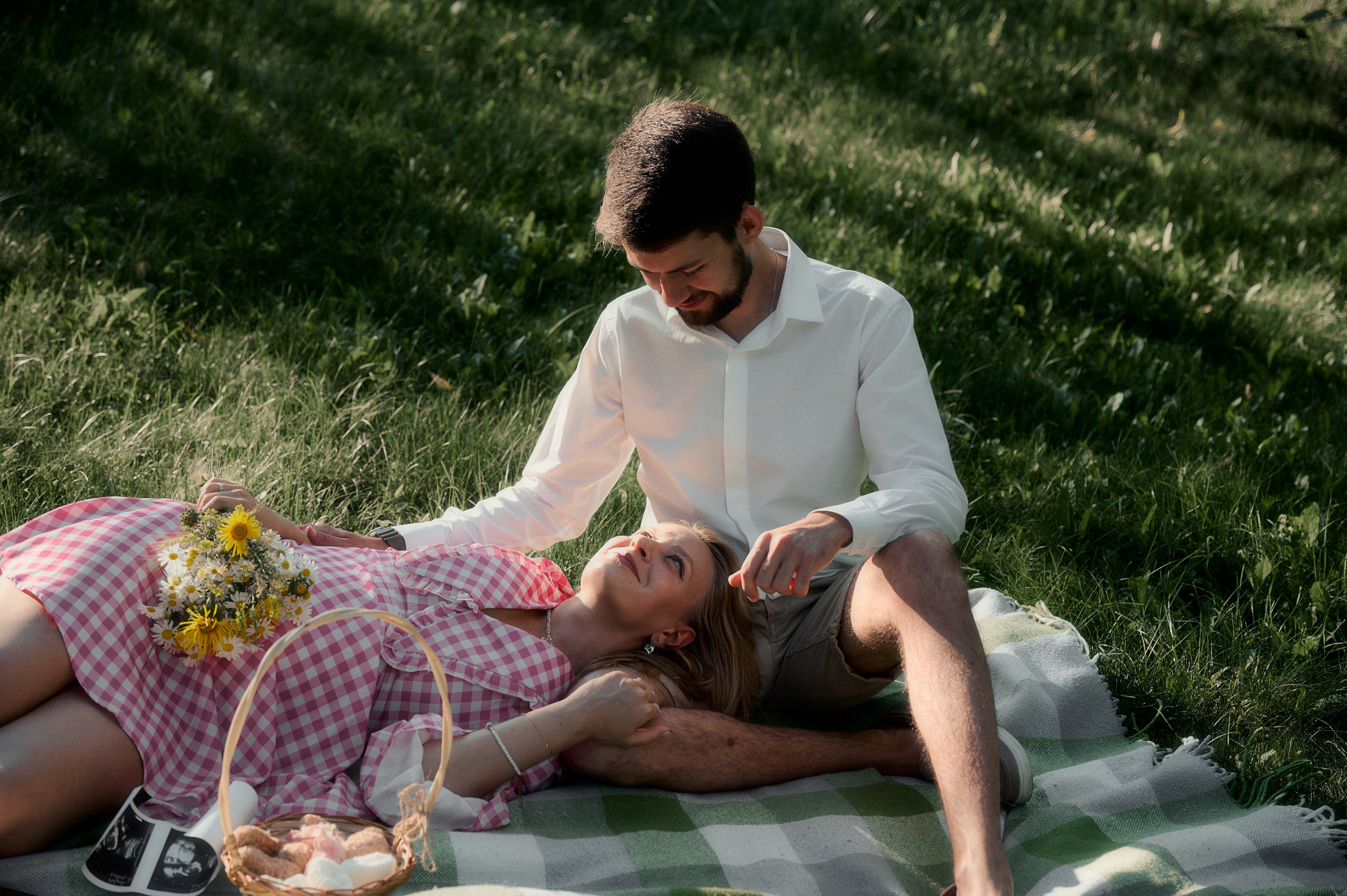 Елизавета лежит на пледе, Юрий сидит рядом, на пледе корзина с цветами.