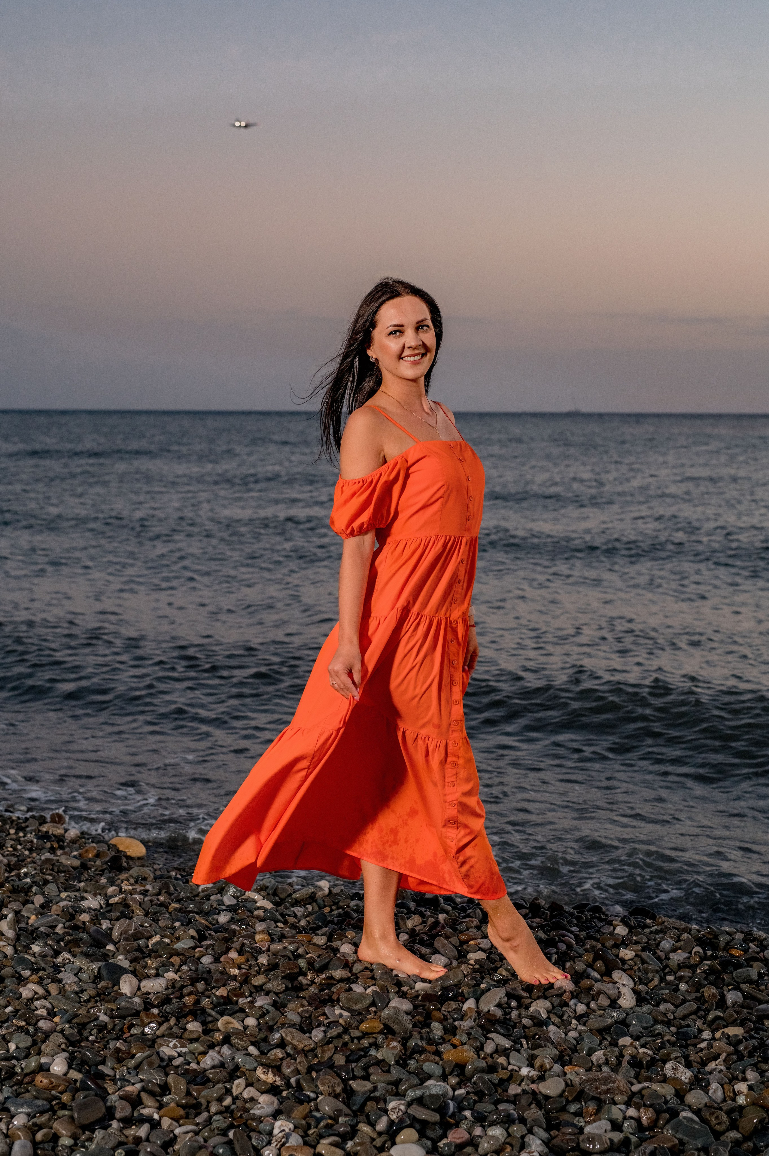 девушка на закате в оранжевом платье гуляет у моря в Сочи