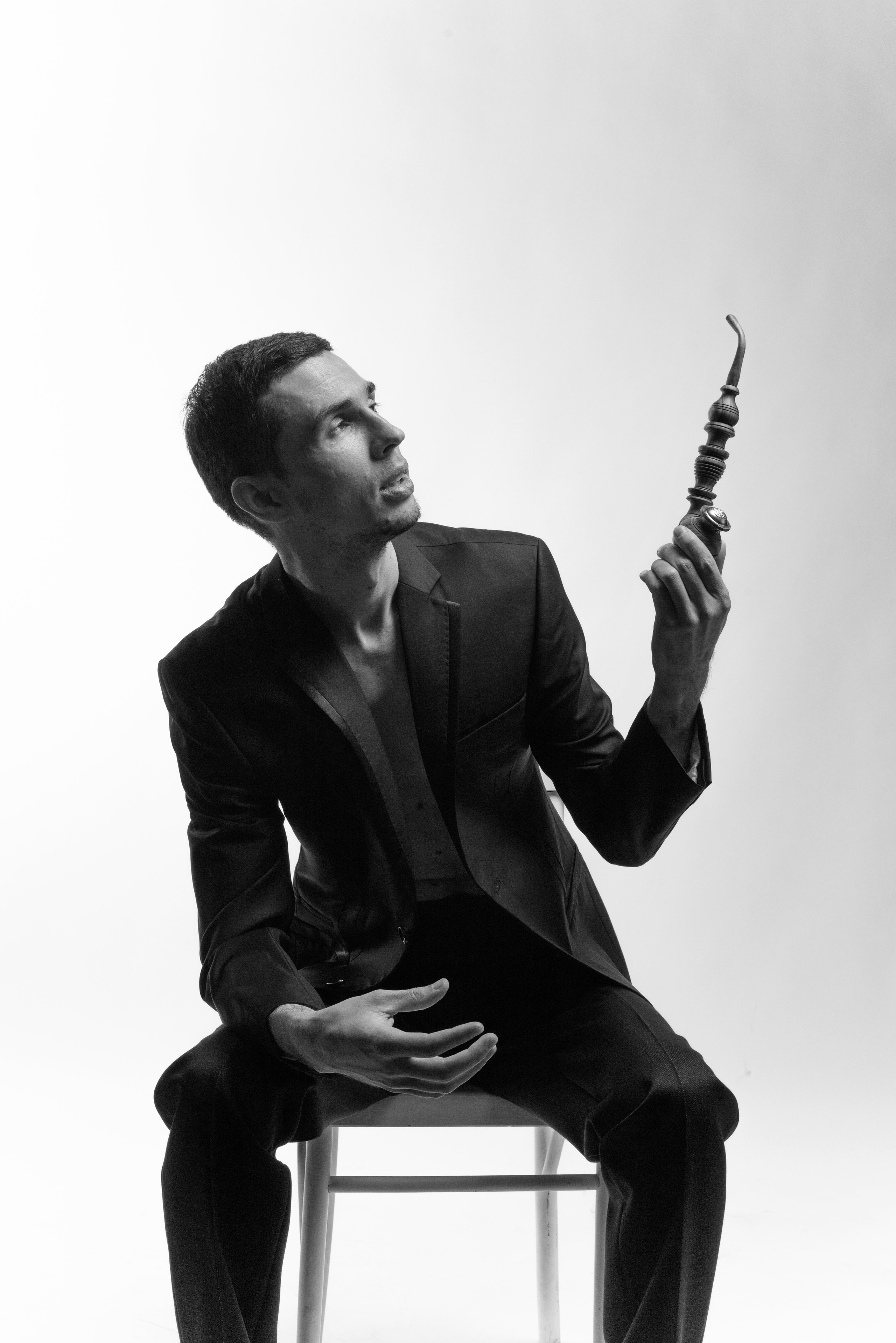 Мужской студийный портрет. Мужчина сидит на стуле на белом фоне и держит в руках трубку