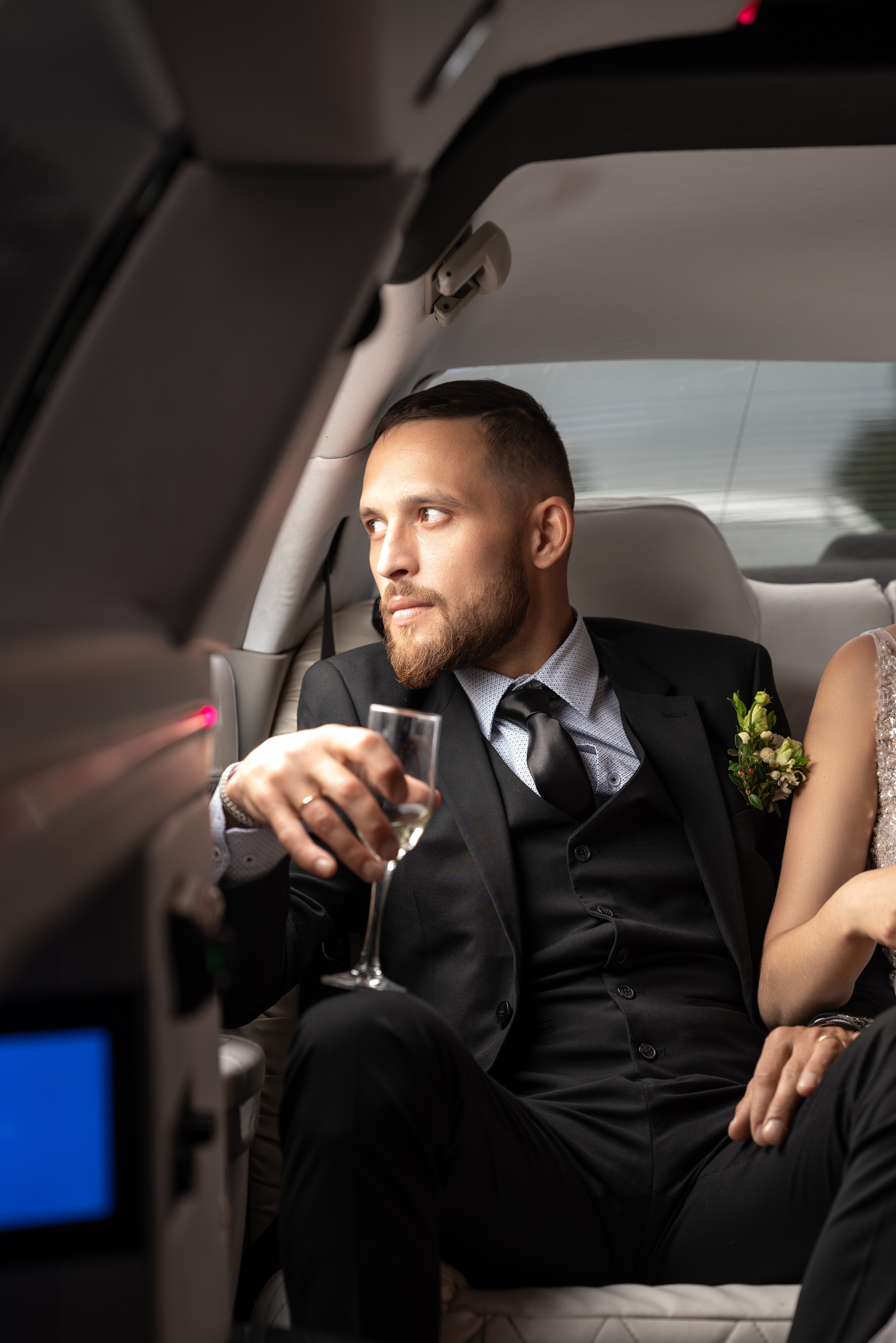 жених в лимузине с фужером шампанского смотрит в окно.