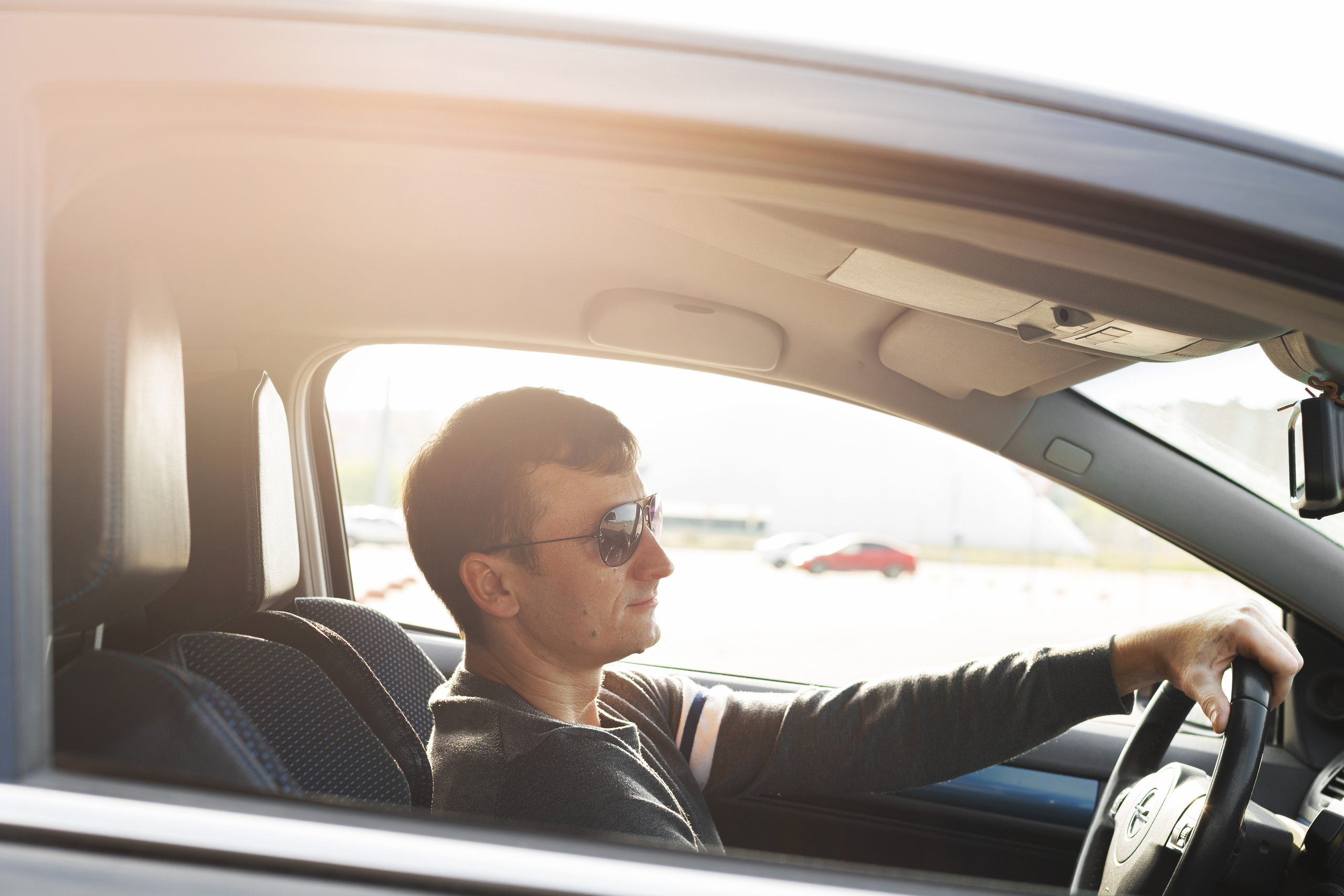 Съемка в стиле форсаж. Мужчина сидит в машине, руки на руле, солнце светит в кадр