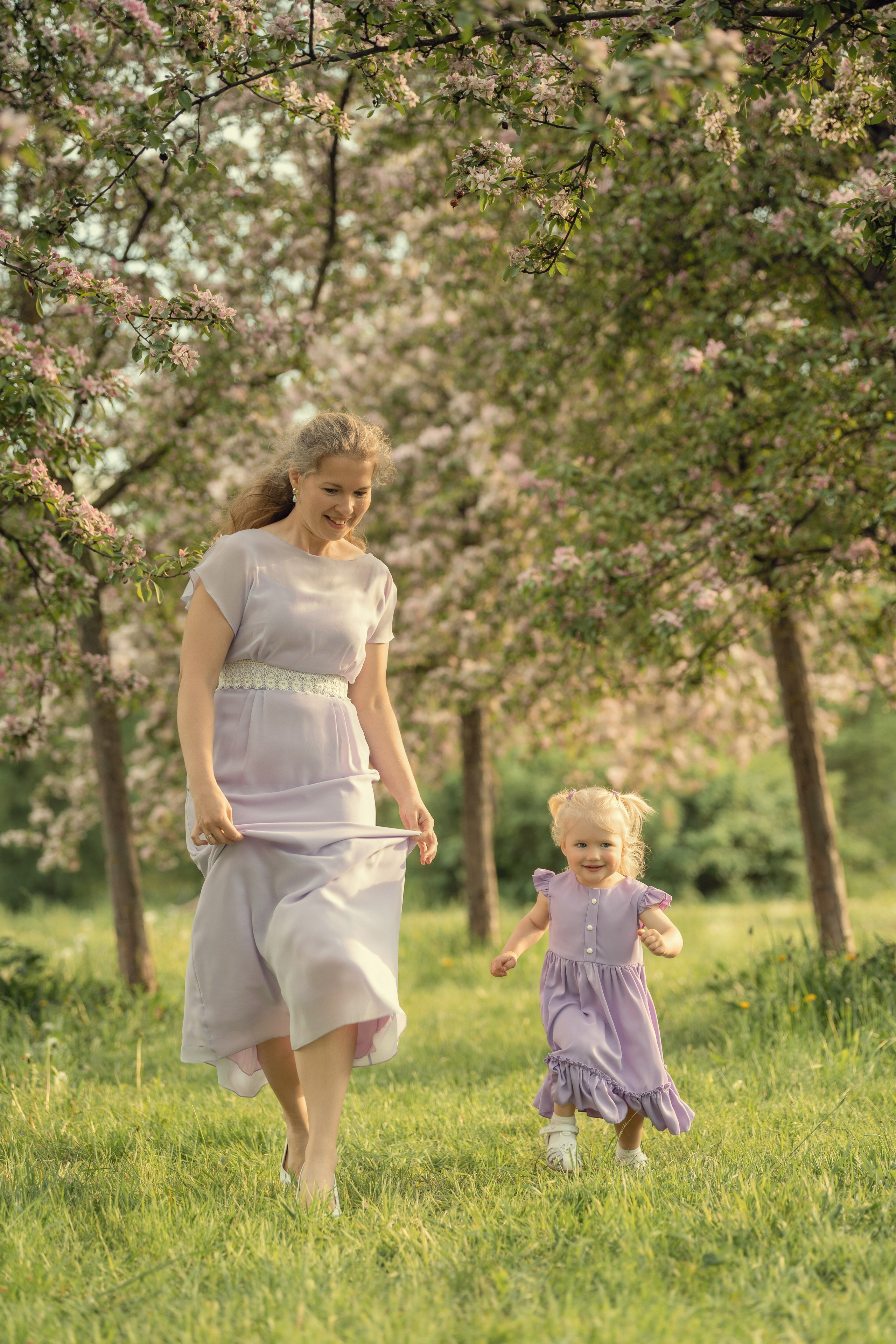 Мама с маленькой дочкой бегут по саду