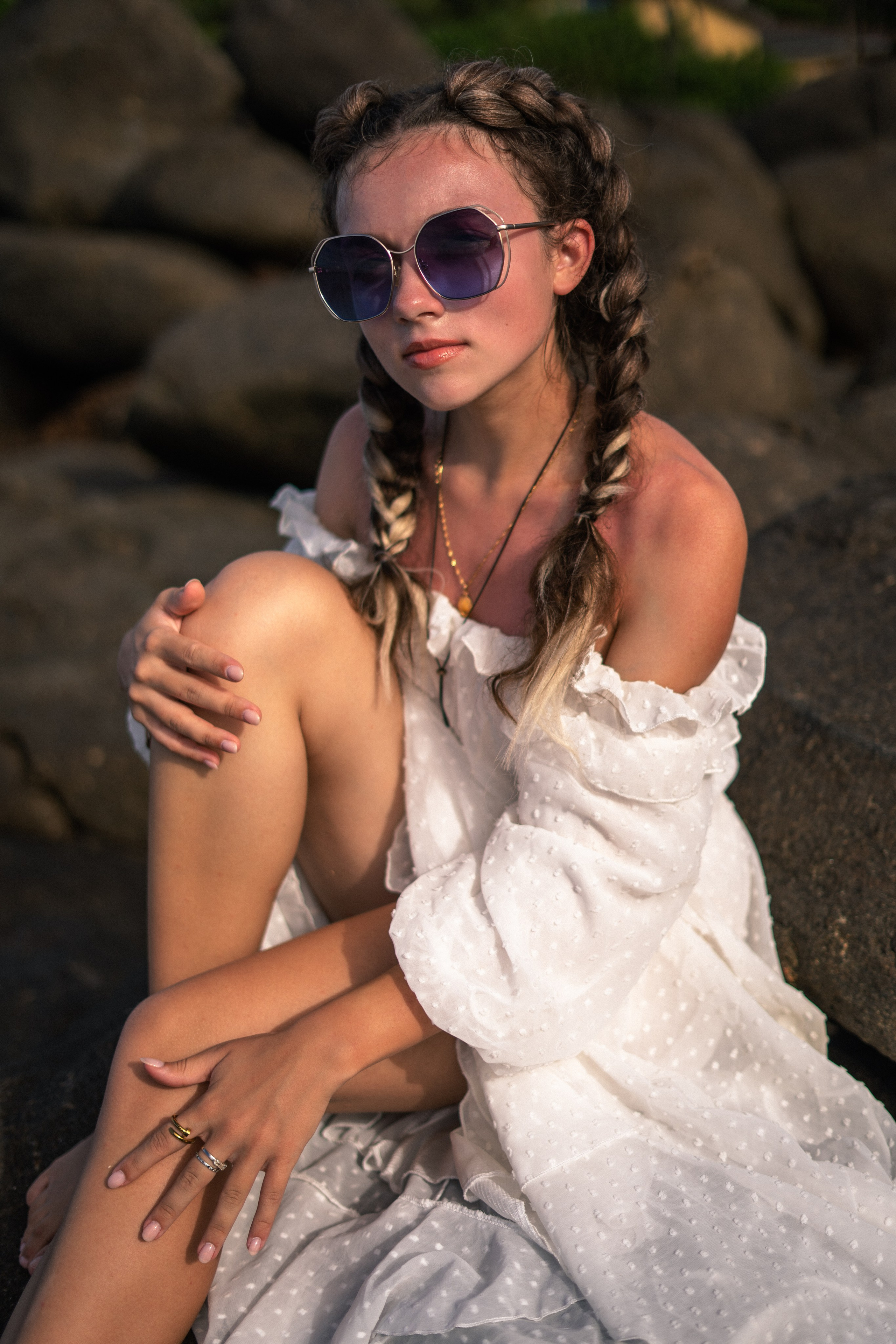 photoshoot of a young girl in a white dress and glasses on the rocks by the ocean
