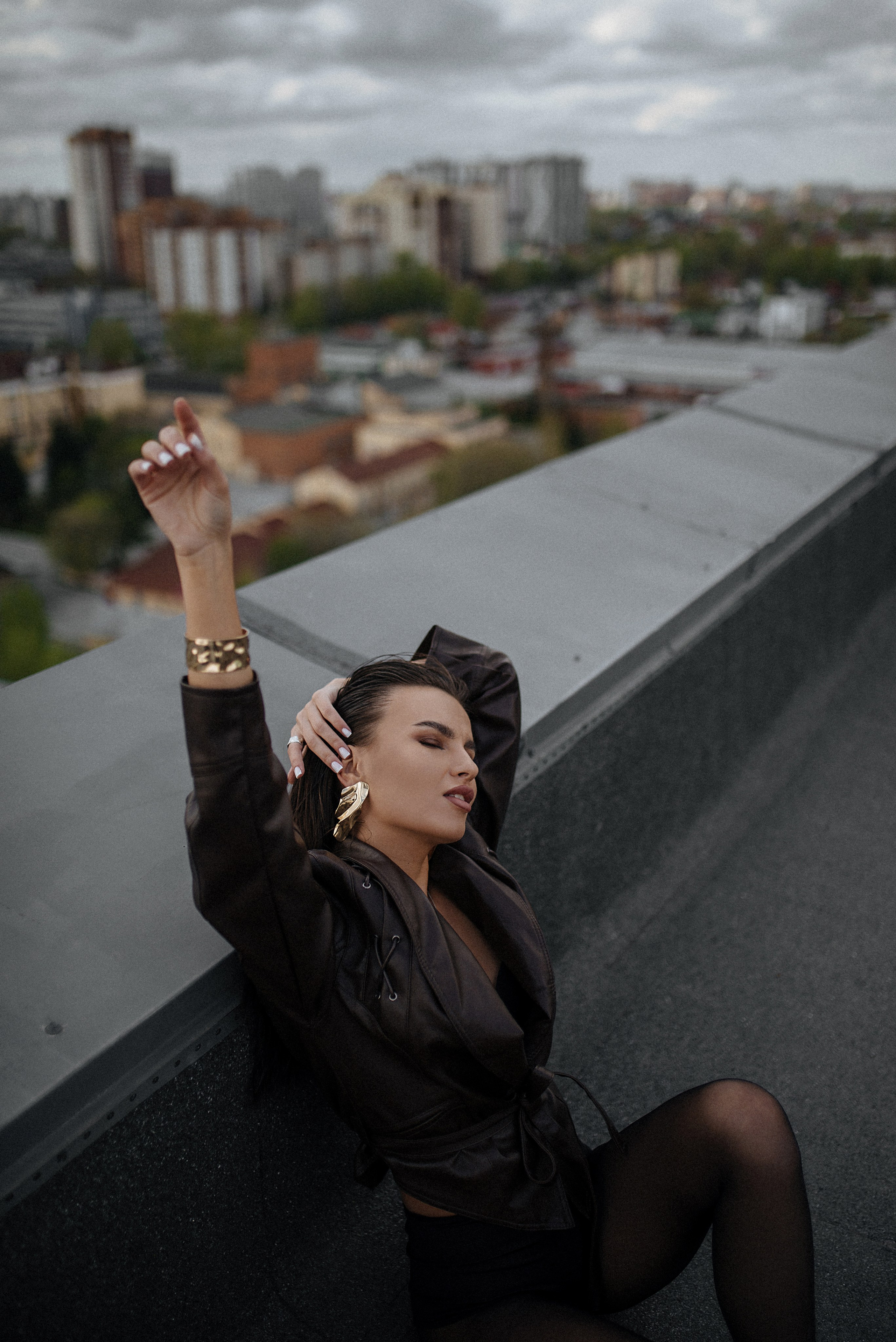Индивидуальная фотосессия на крыше Новосибирск. Девушка в кожанке и колготках сидит на крыше с видом на Новосибирск, с закрытыми глазами.