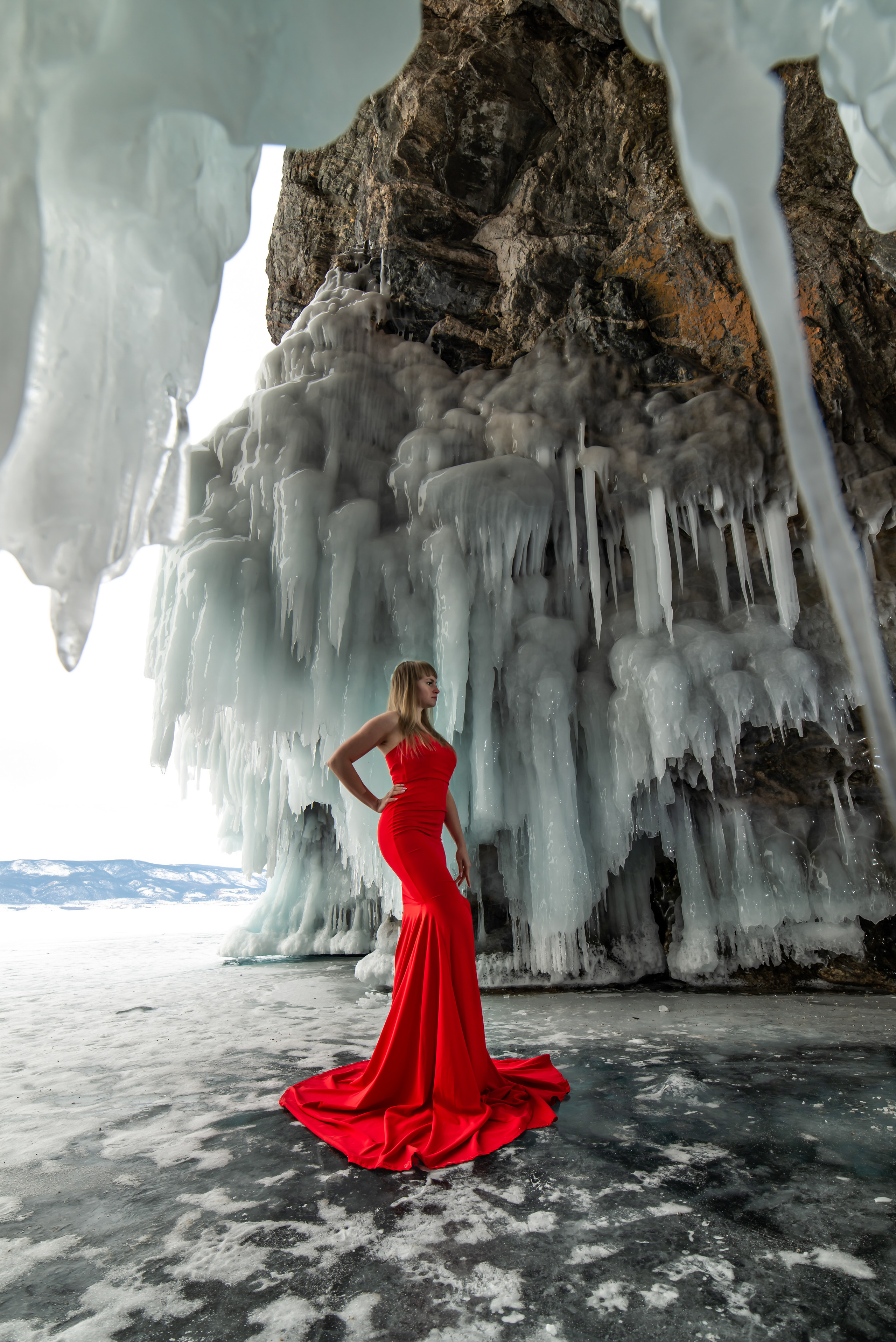 Девушка в красном облегающем силуэтном платье русалке в ледяном гроте на байкале