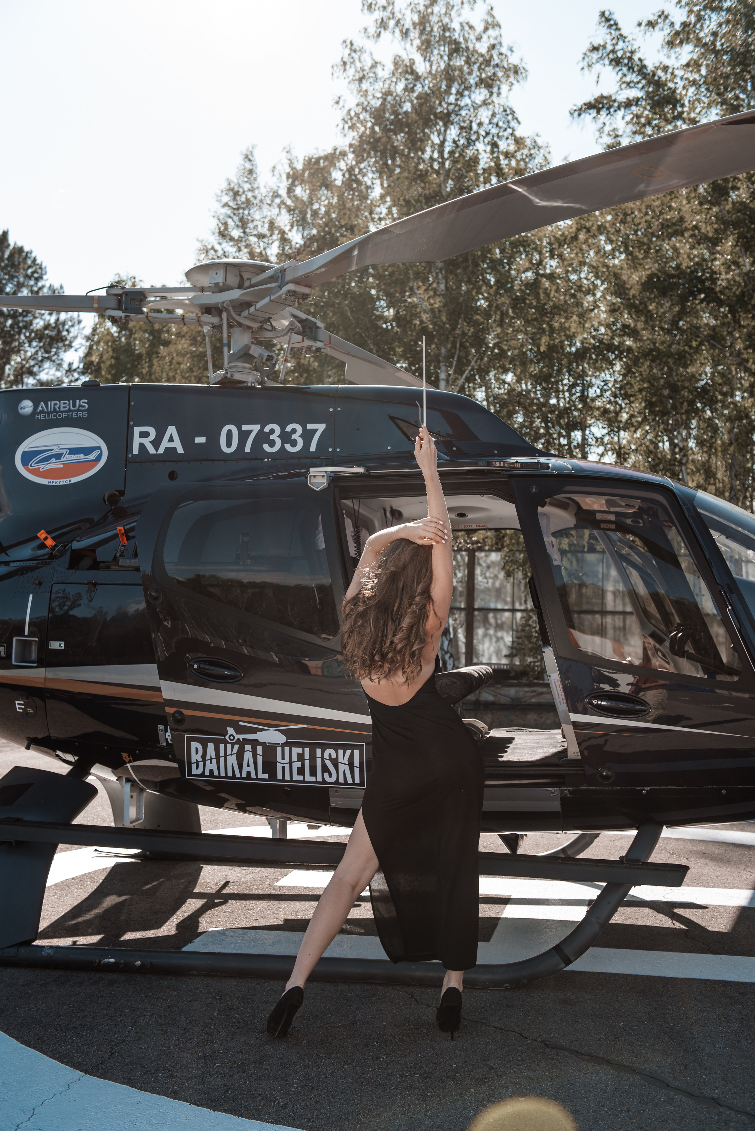 Девушка бонда в черном платье стоит спиной у вертолета