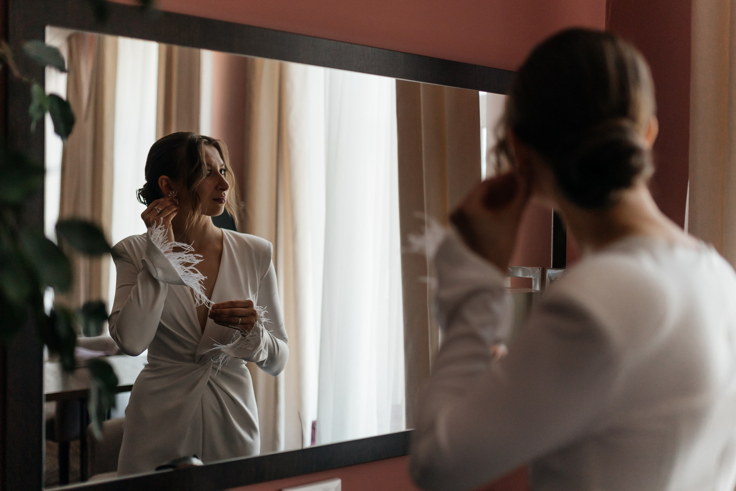 Девушка смотрит в зеркало и поправляет серьгу на ухе