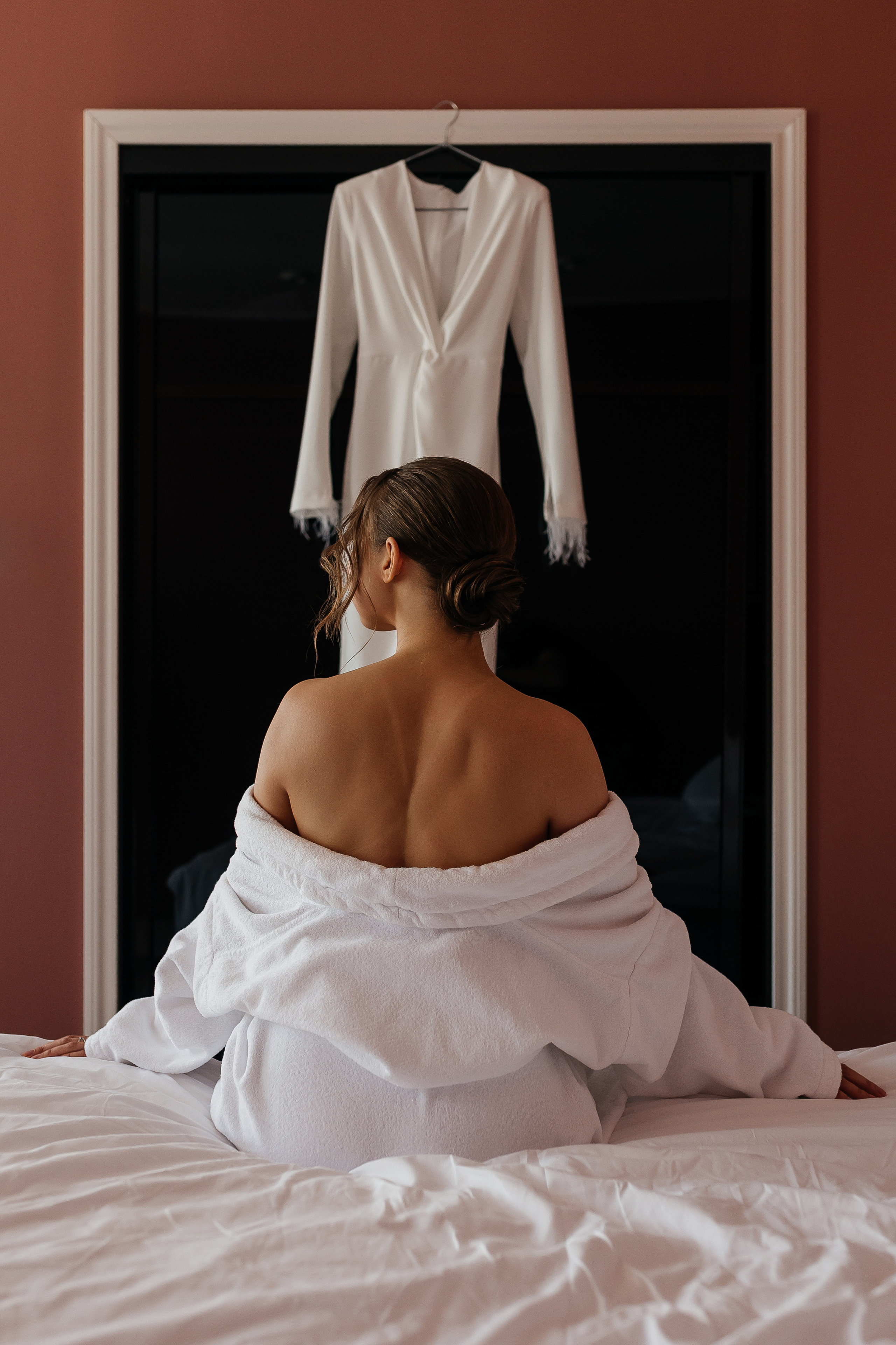 Невеста сидит на кровати в отеле и смотрит на свадебное платье