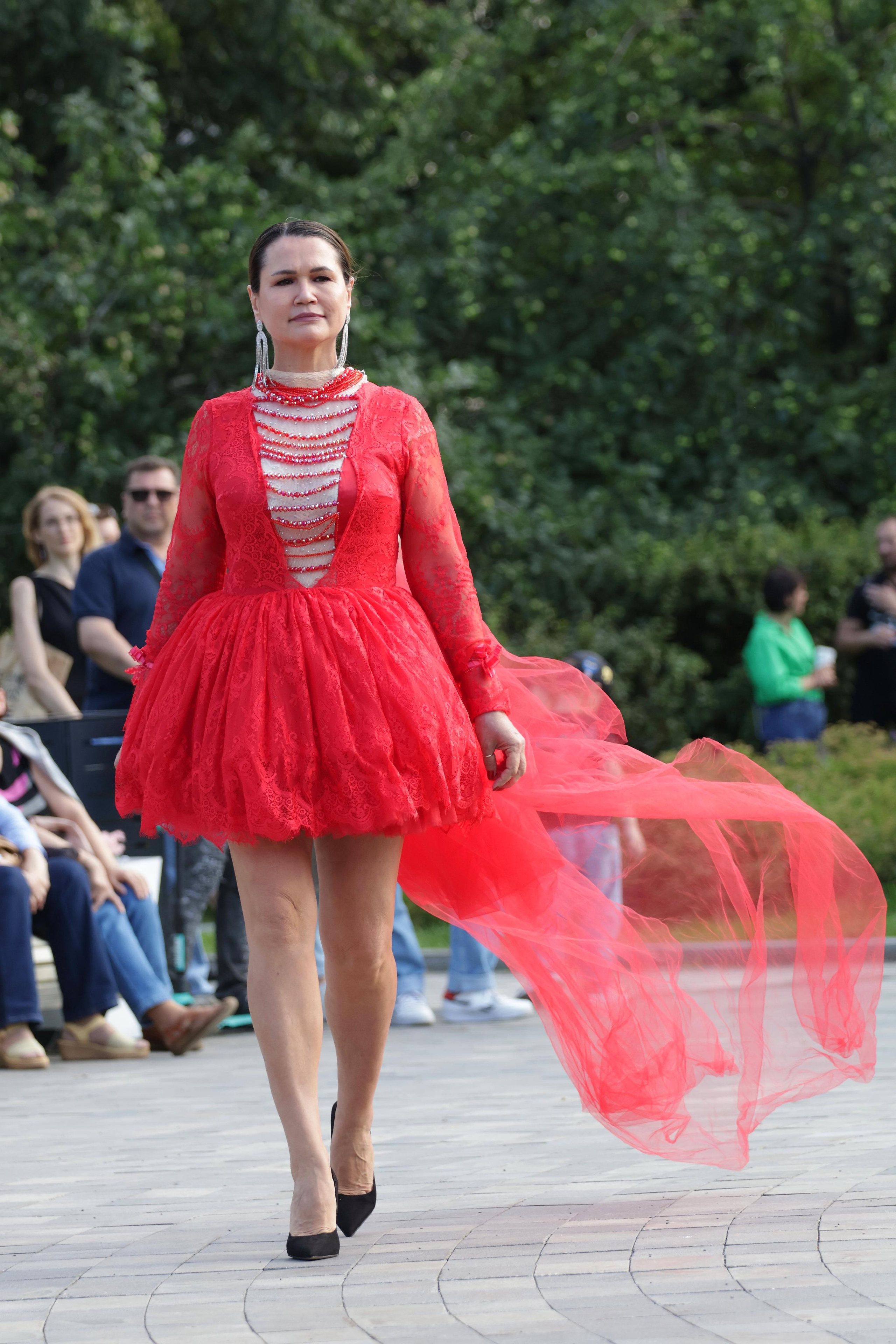 Девушка демонстрирует красное платье на показе в саду имени Баумана