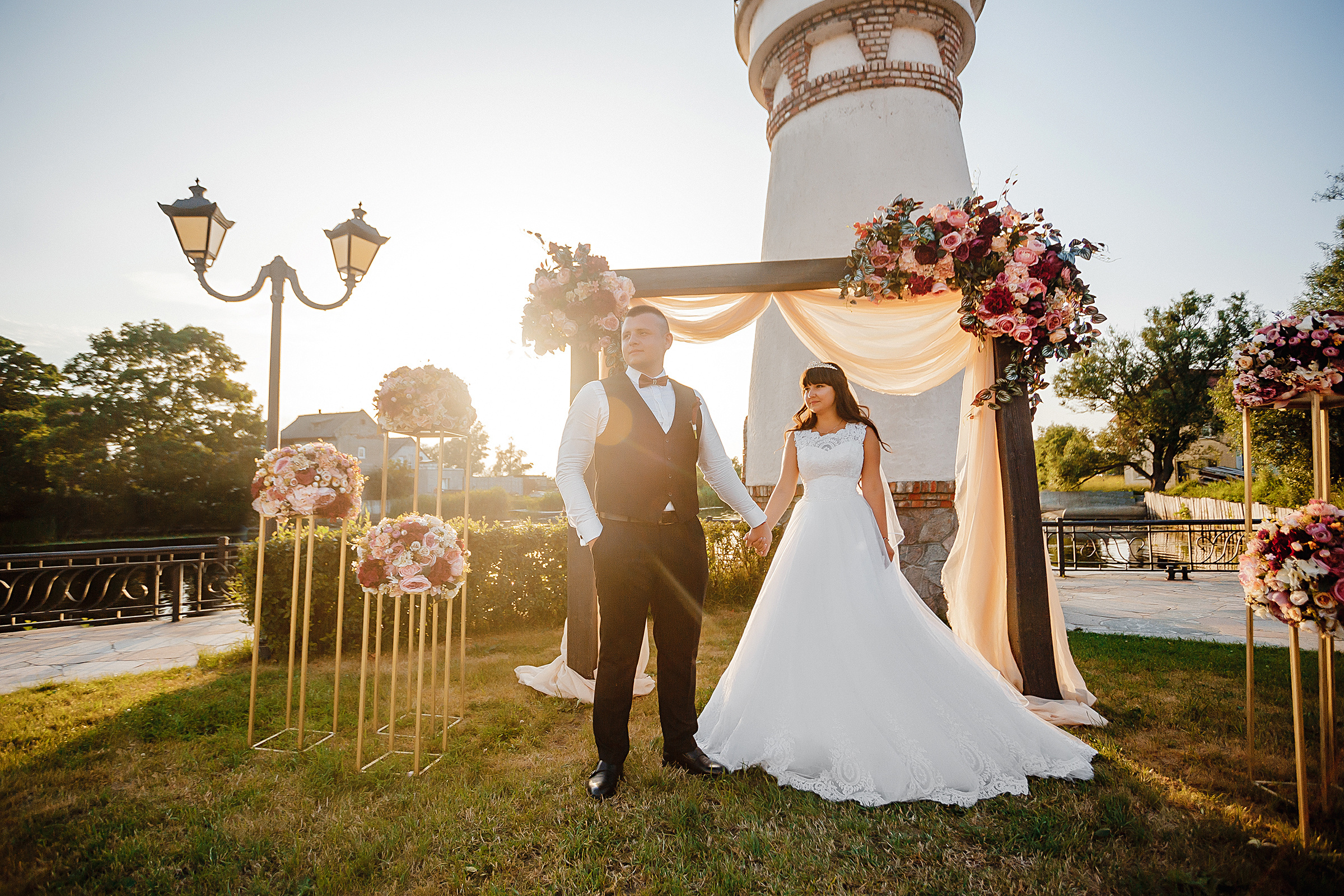 Жених держит невесту за руку у арки выездной регистрации