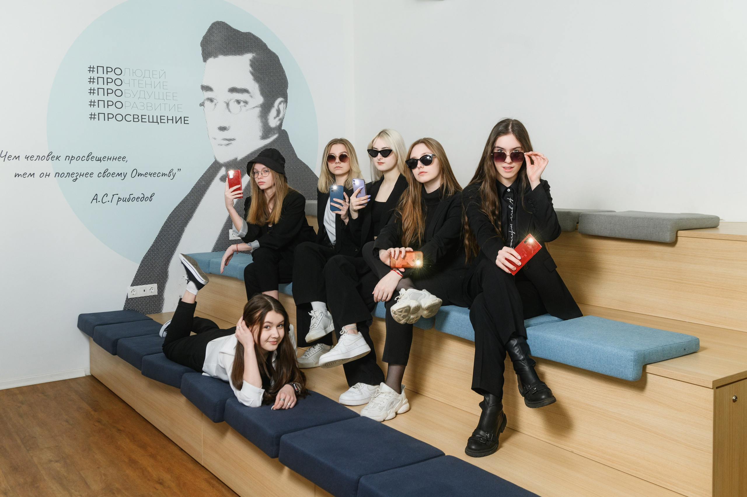 Компания старшеклассниц позирует на многоуровневых скамьях в современном светлом интерьере.