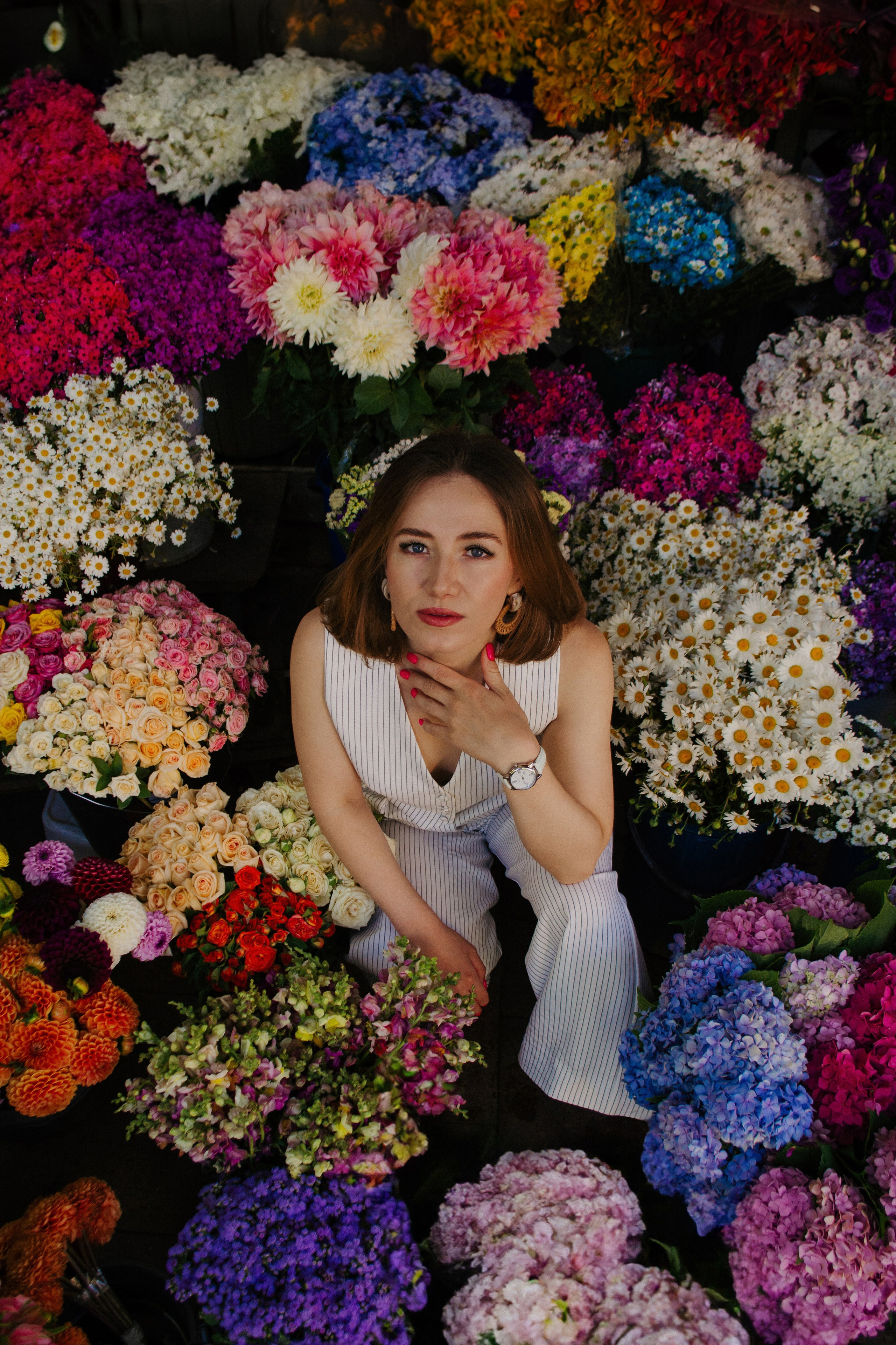 Снимок девушки в белом костюме, окруженной огромным количеством разных ярких цветов. Вид сверху