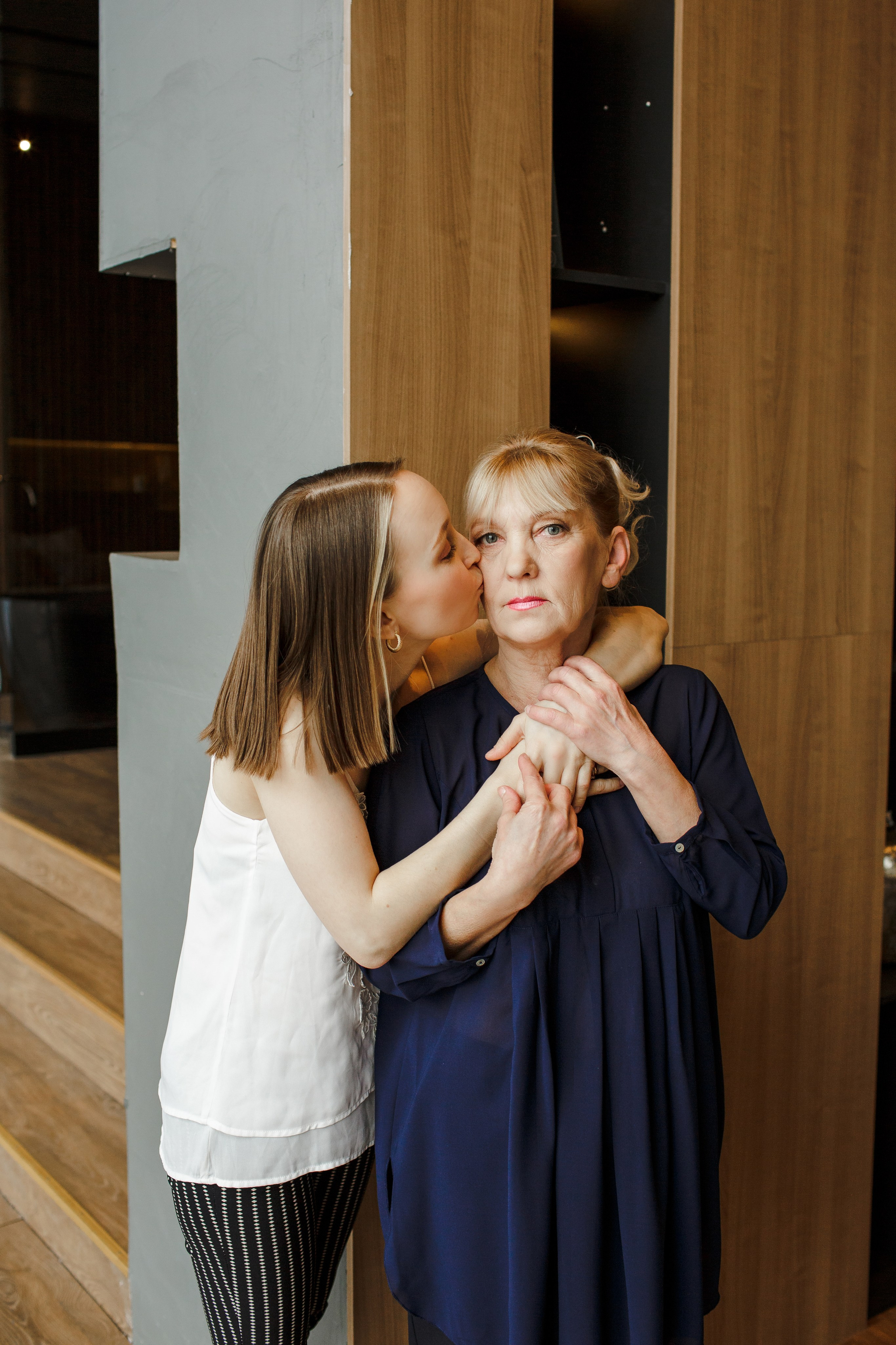 Дочка целует маму в щеку на семейной фотосессии в студии.